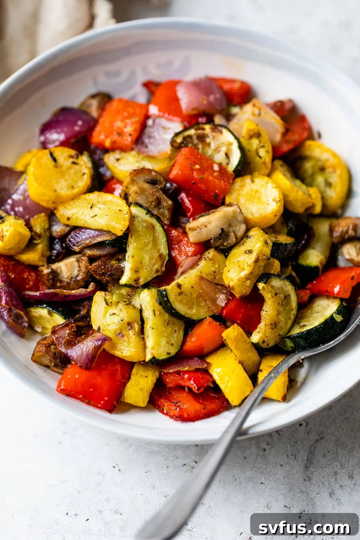 A vibrant bowl of roasted air fryer vegetables, perfectly tender and caramelized, with a serving spoon tucked in. Ideal for a healthy and quick side dish.