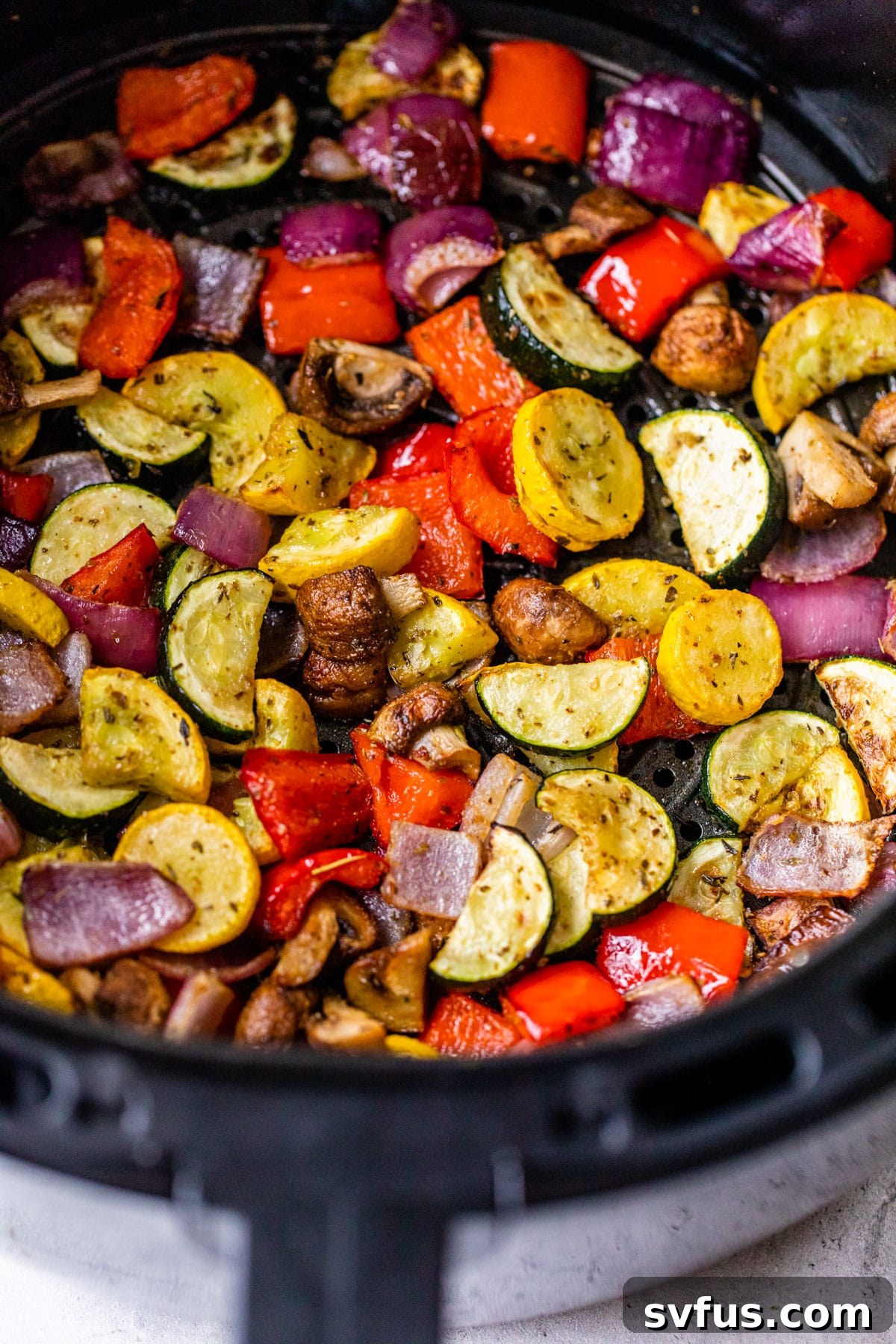 A close-up view of a batch of freshly roasted vegetables, vibrant and perfectly cooked, nestled within an air fryer basket.