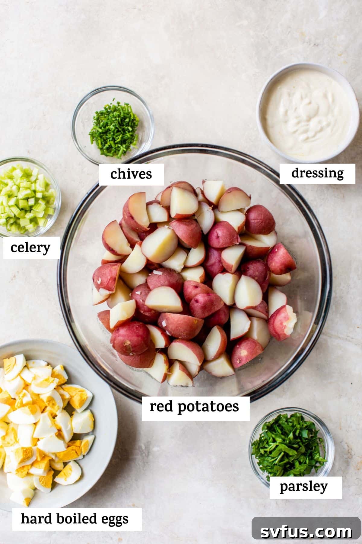 All the fresh ingredients for healthy potato salad laid out on a table in small bowls, including red potatoes, hard-boiled eggs, fresh herbs, and dressing components.