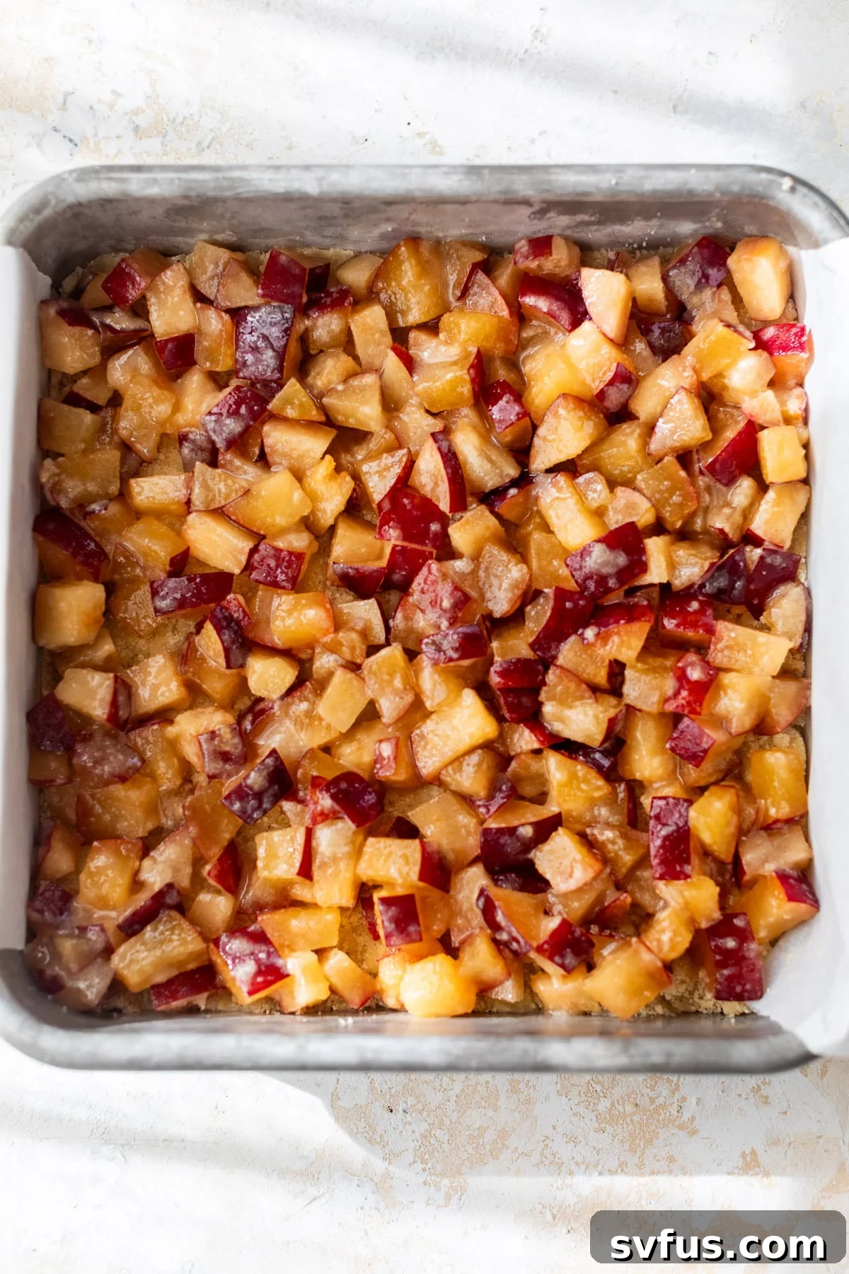A vibrant close-up of diced plum filling, perfectly arranged in a baking dish, ready for the top crumb layer.