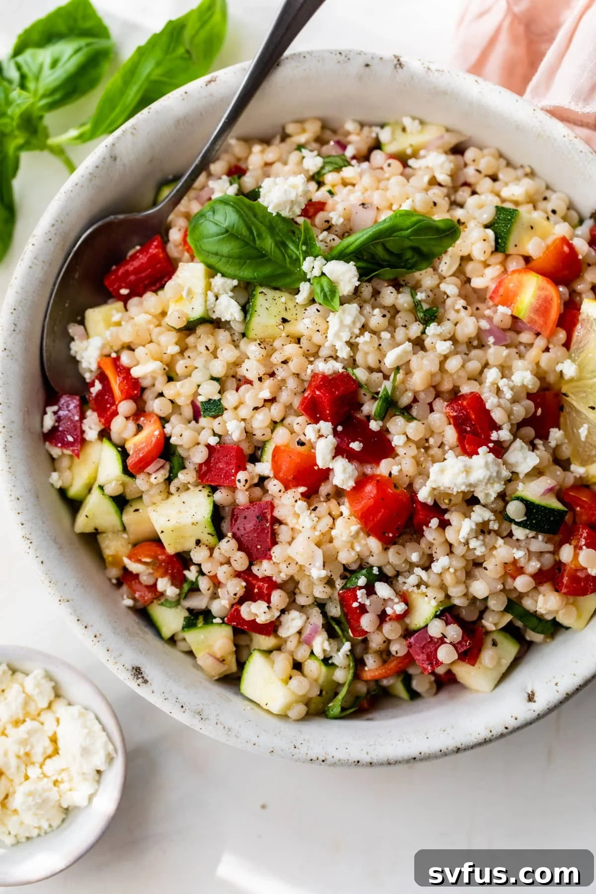 A beautifully arranged bowl of vibrant vegetable couscous with a spoon, ready to be served.