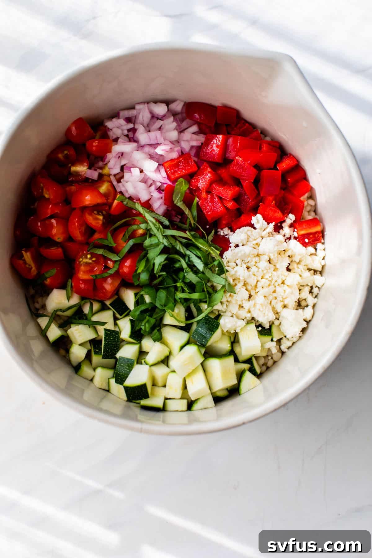 All the freshly chopped ingredients for vegetable couscous separated in a large mixing bowl, ready for tossing.