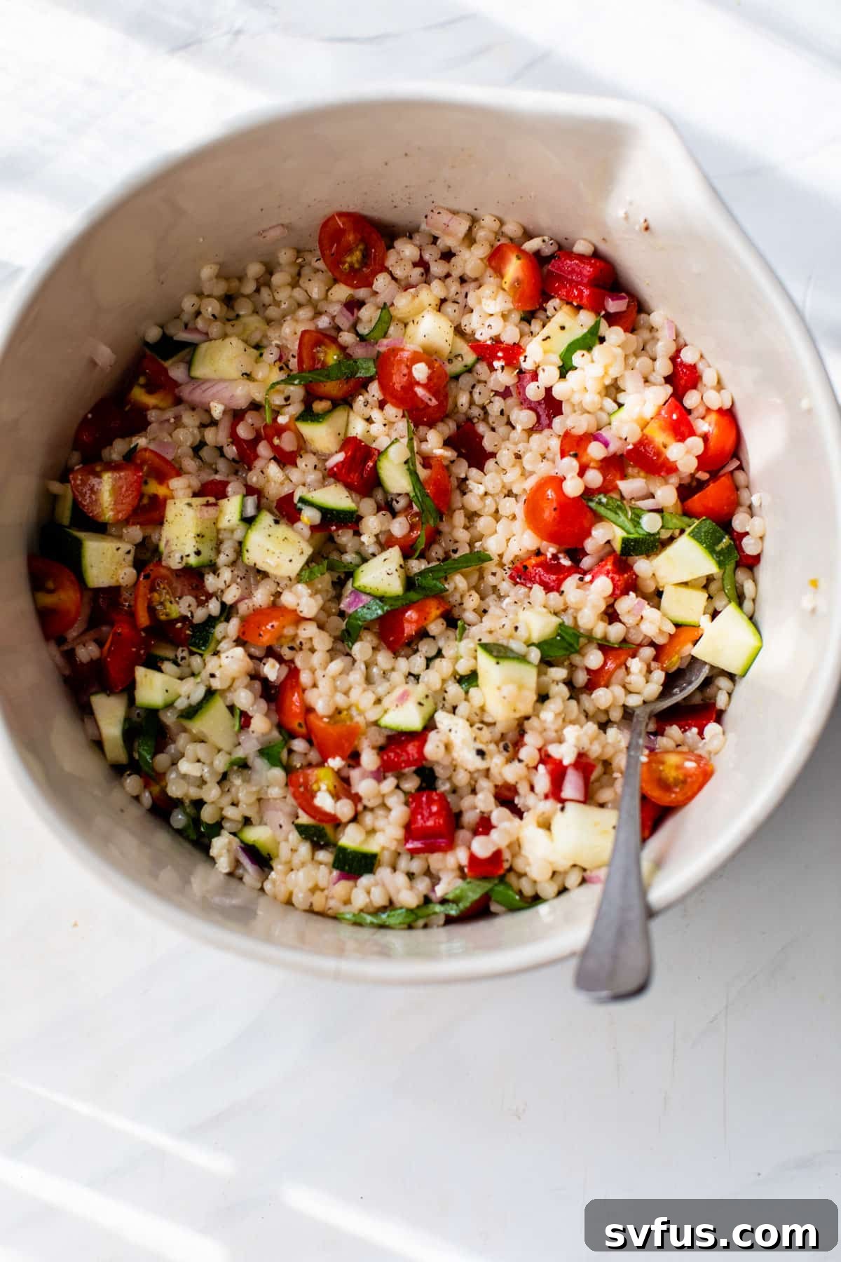The fully assembled vegetable couscous salad in a mixing bowl with a spoon, ready to be enjoyed.