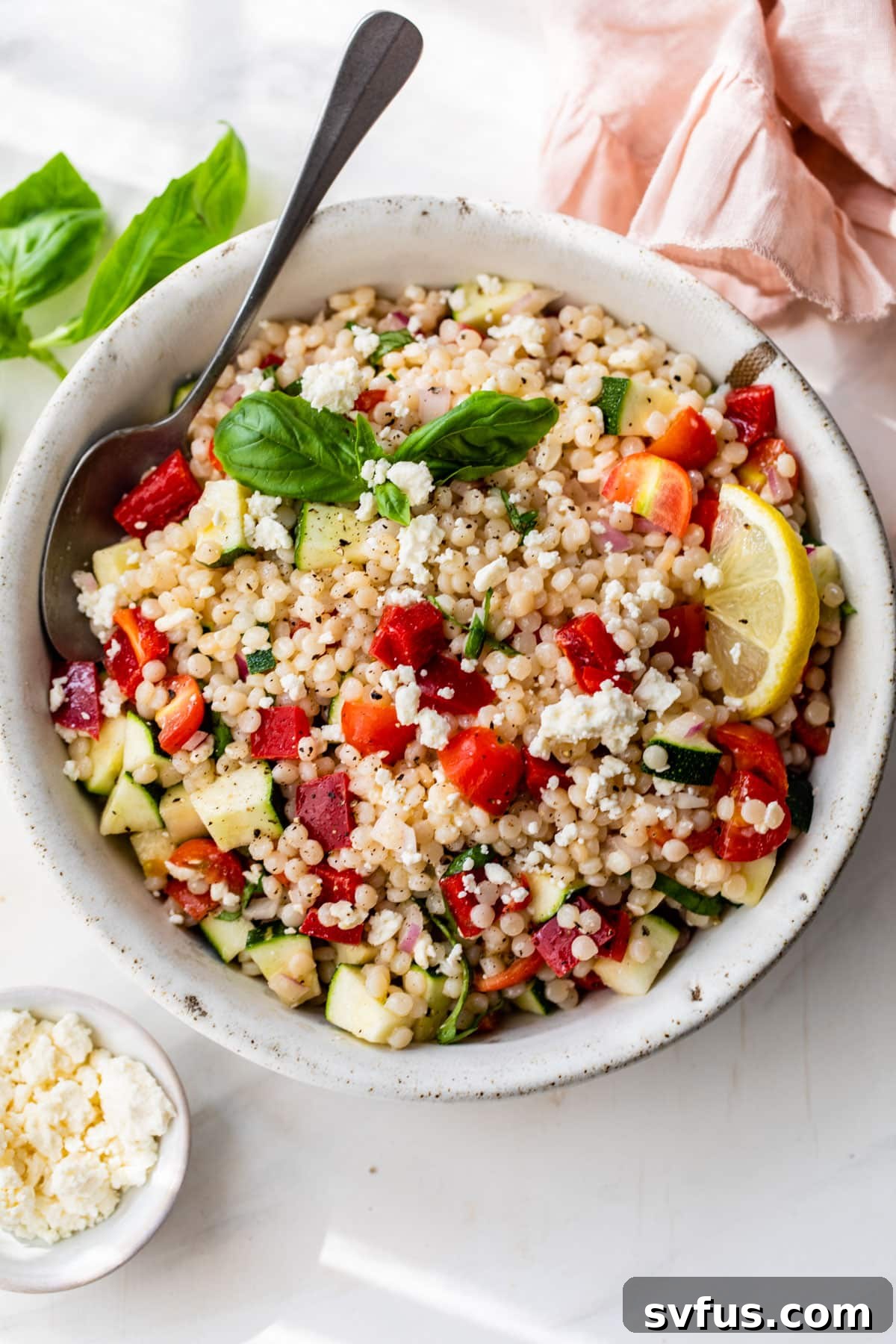 A serving of vegetable couscous salad in a bowl with a spoon, highlighting its vibrant colors and freshness.