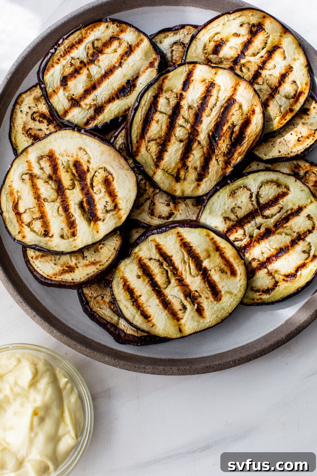 grilled eggplant rounds on a plate with garlic aioli on the side of the plate