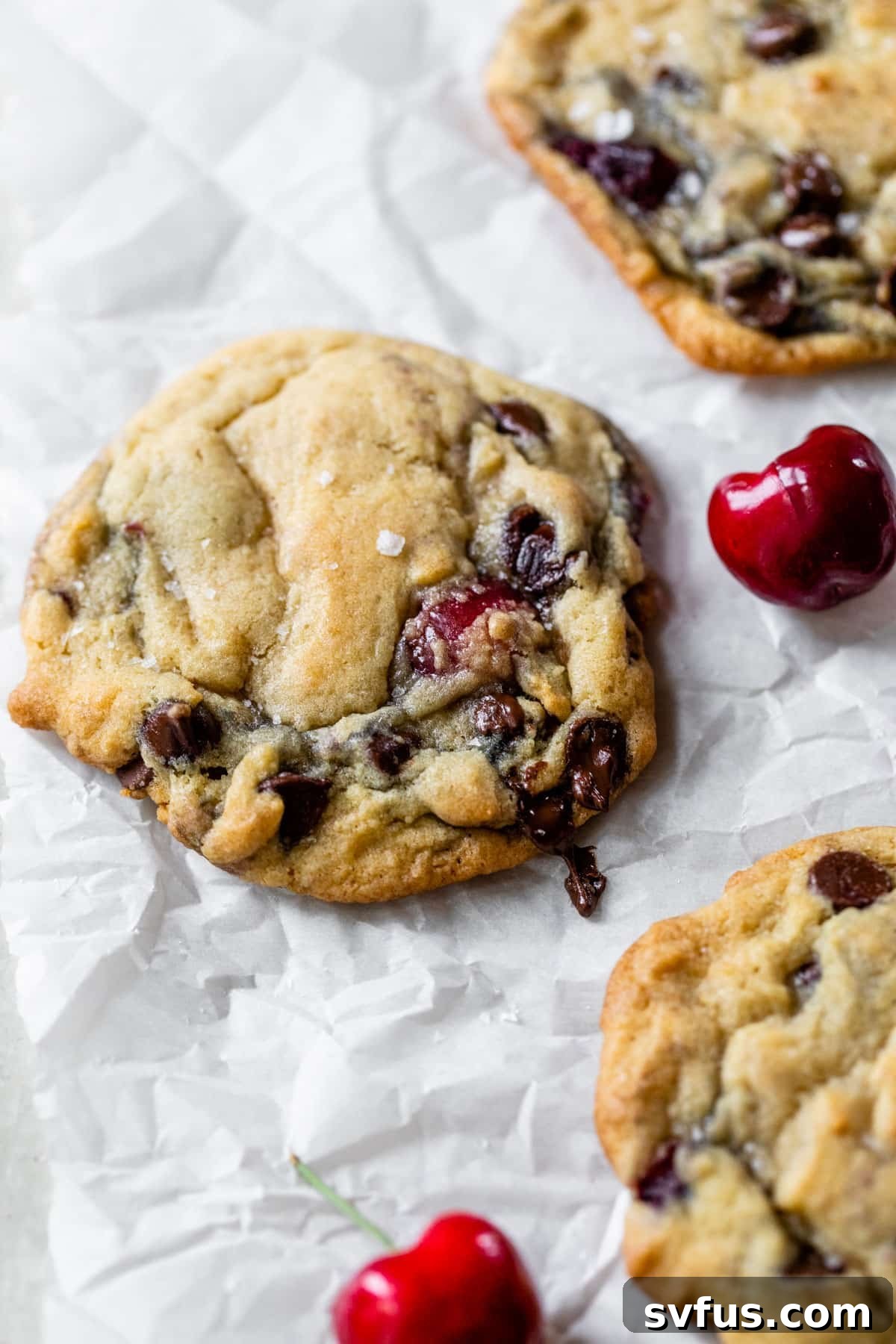 chocolate chip cookies on parchment paper with fresh cherries