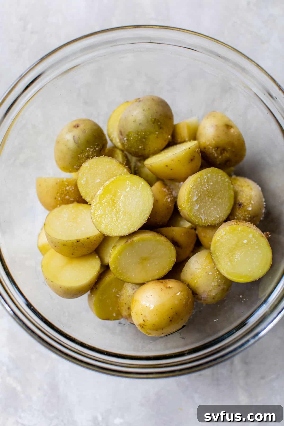 Quartered potatoes in a glass bowl with salt, ready for grilling
