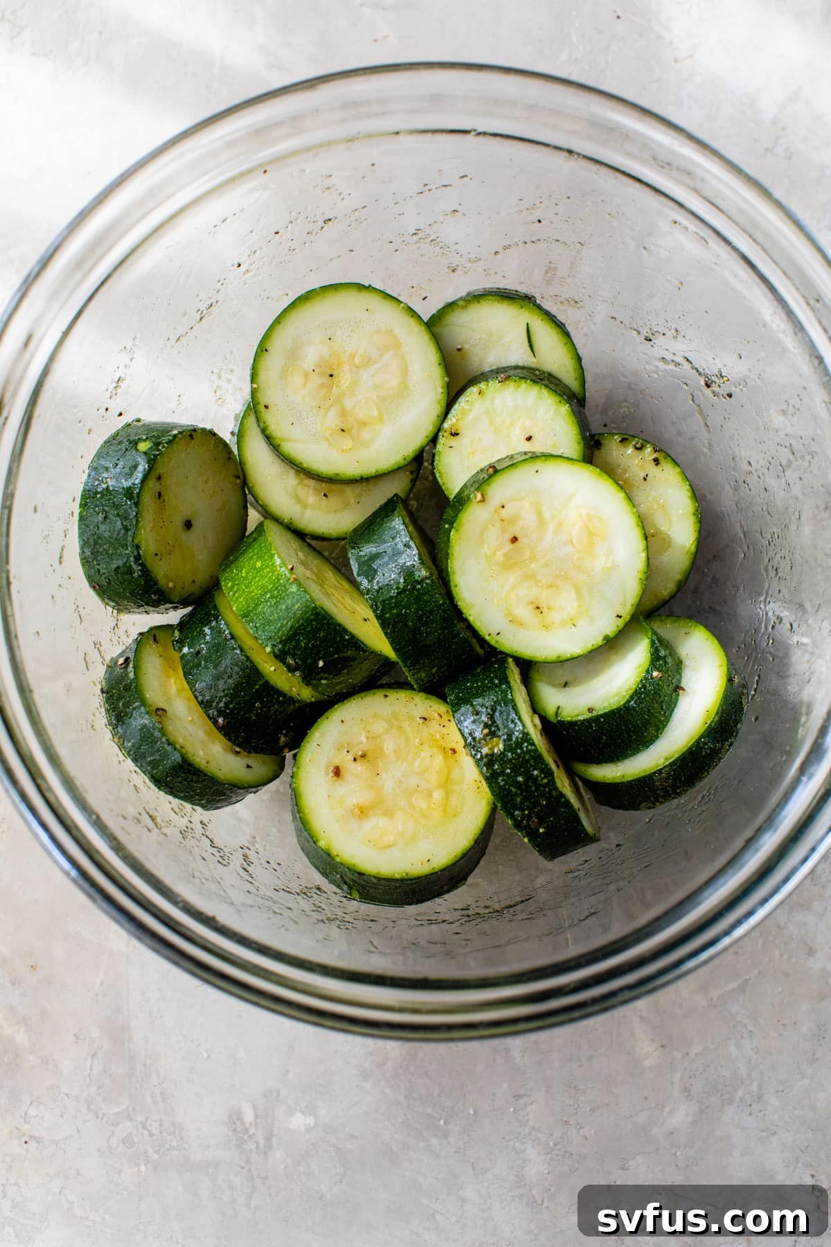 Zucchini slices thoroughly coated in olive oil and seasonings in a glass bowl