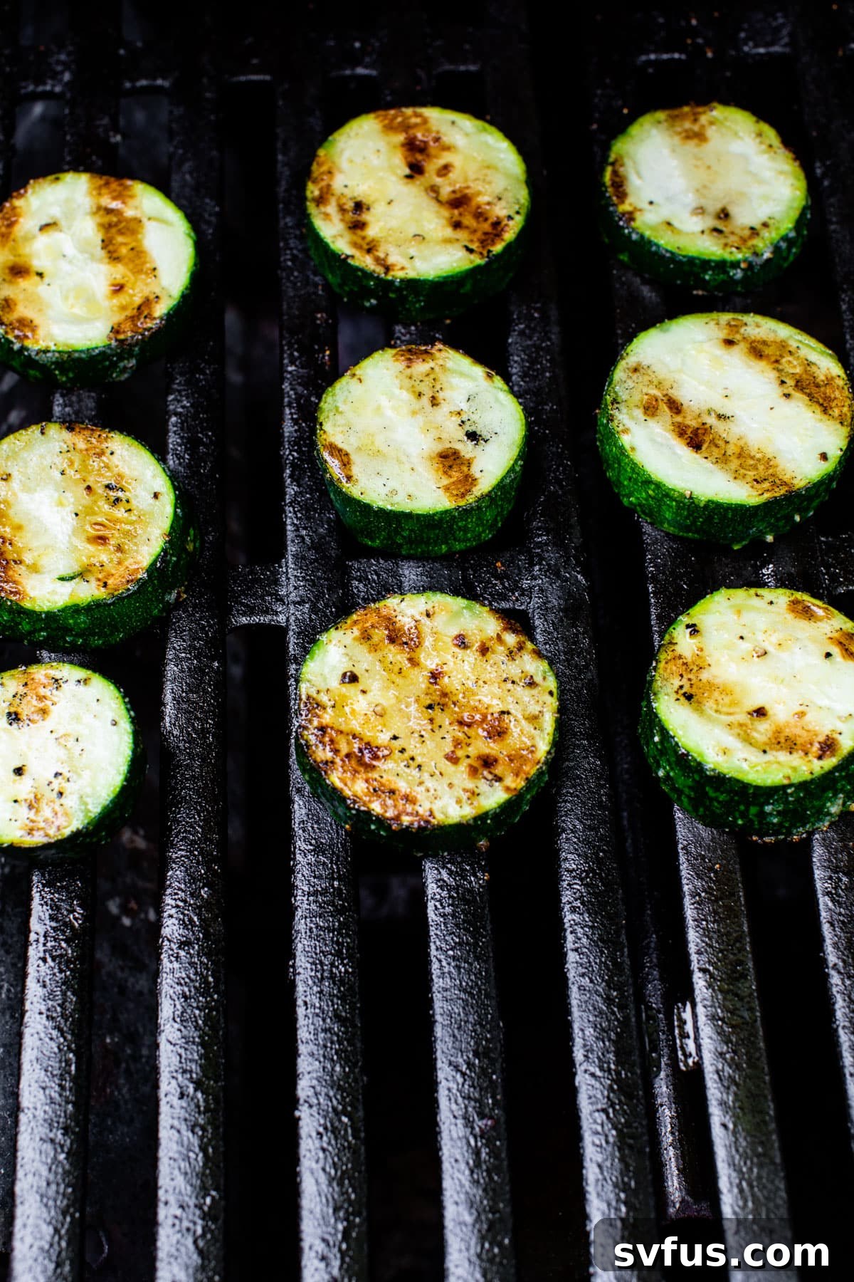 Zucchini slices cooking on a hot grill, showing developing char marks