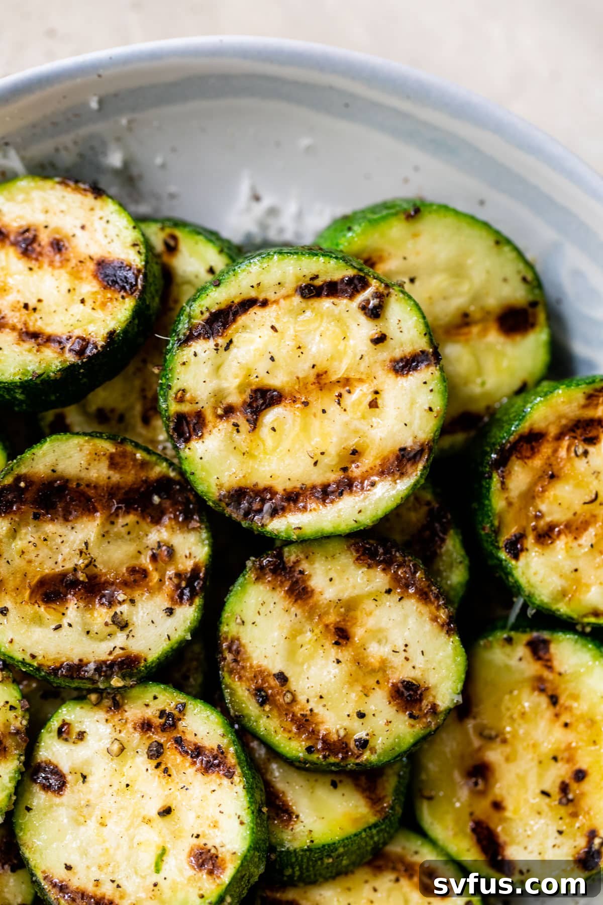 A close-up shot of perfectly grilled zucchini slices in a bowl, showing texture and seasoning