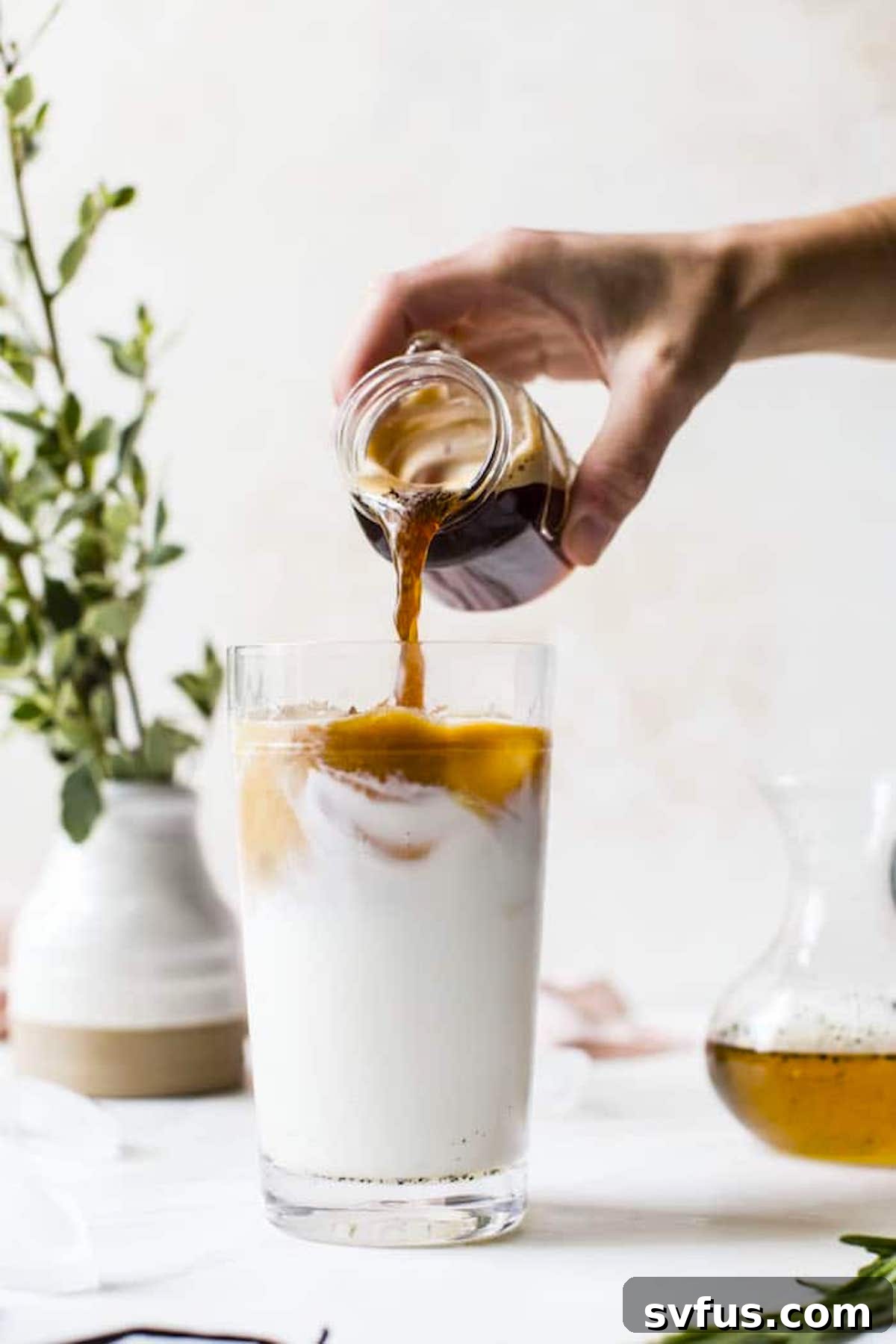 A close-up of a beautifully layered iced vanilla rosemary latte, showcasing the coffee, milk, and syrup, garnished with a fresh rosemary sprig.