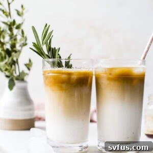Two perfectly poured iced vanilla rosemary lattes, served in tall glasses, garnished with fresh rosemary sprigs.