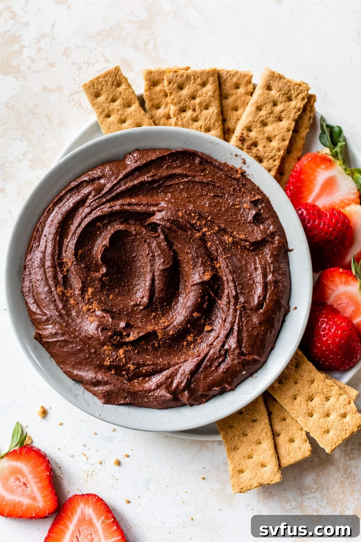 a bowl of chocolate hummus surrounded by graham crackers and sliced strawberries