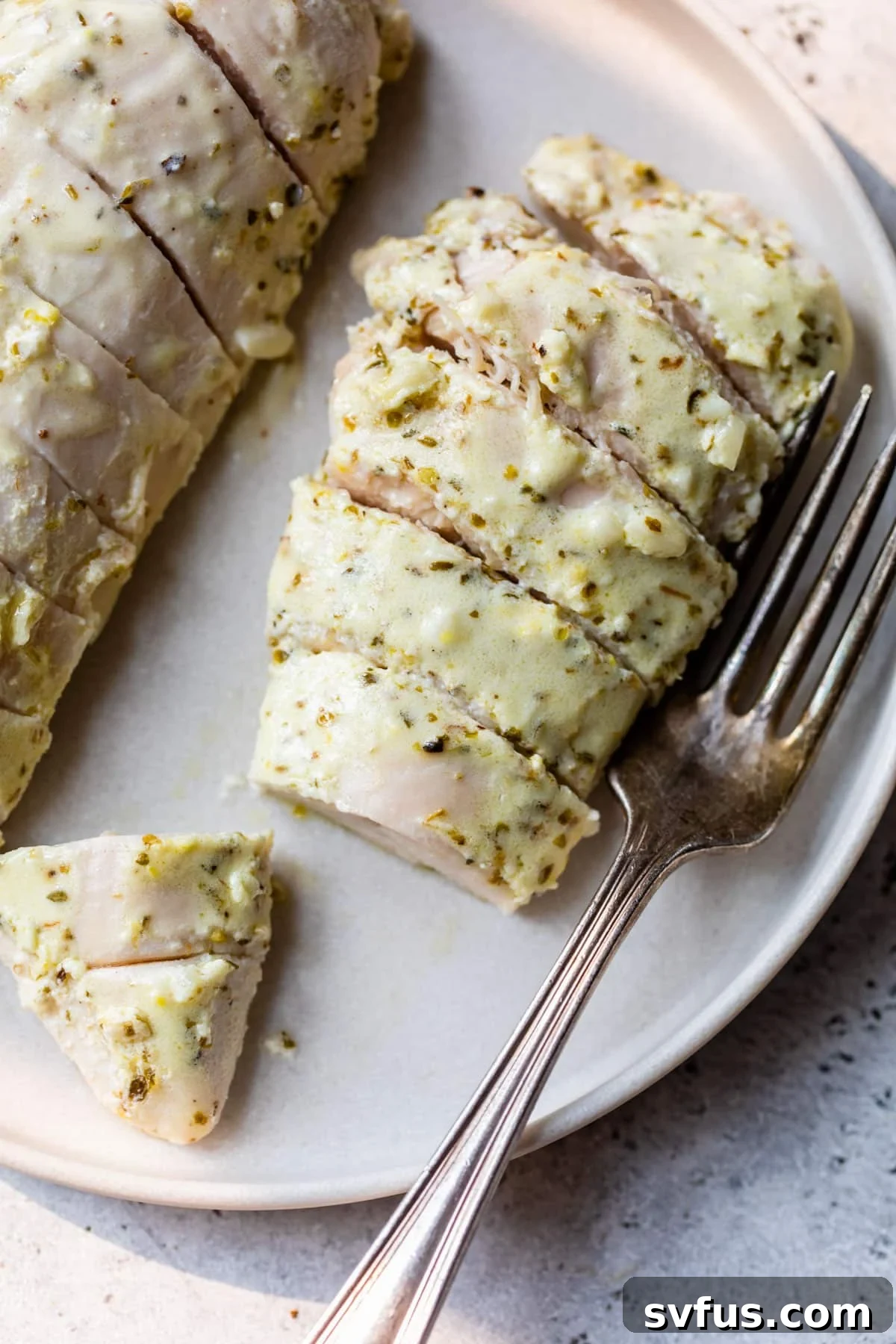 Two perfectly sliced Greek chicken breasts on a plate, ready to be served, with a fork beside them, showcasing their tender, juicy texture and herb-infused skin.