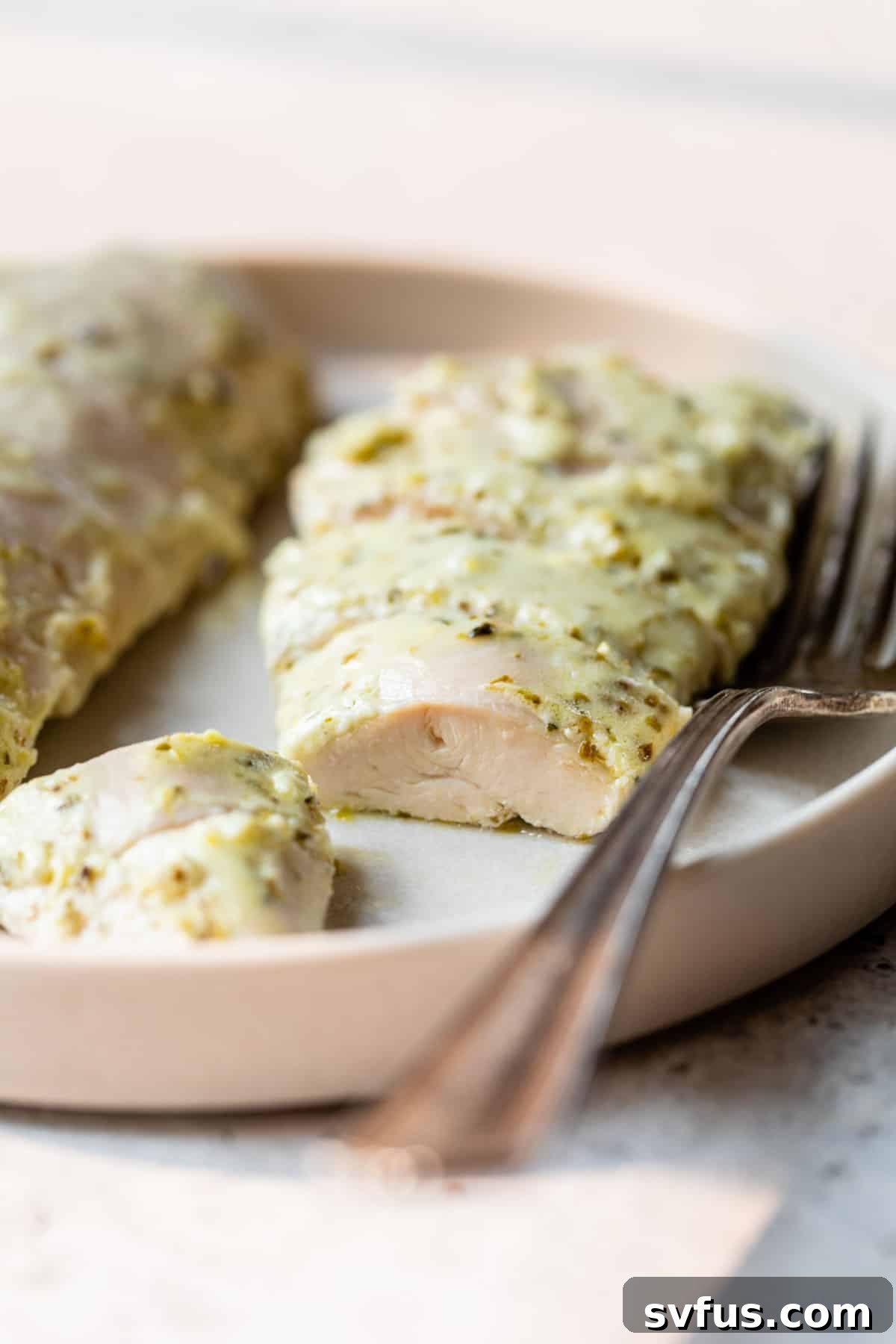 A close-up shot of a perfectly cooked, sliced Greek chicken breast, revealing its juicy interior and golden-brown exterior, resting beside a fork.