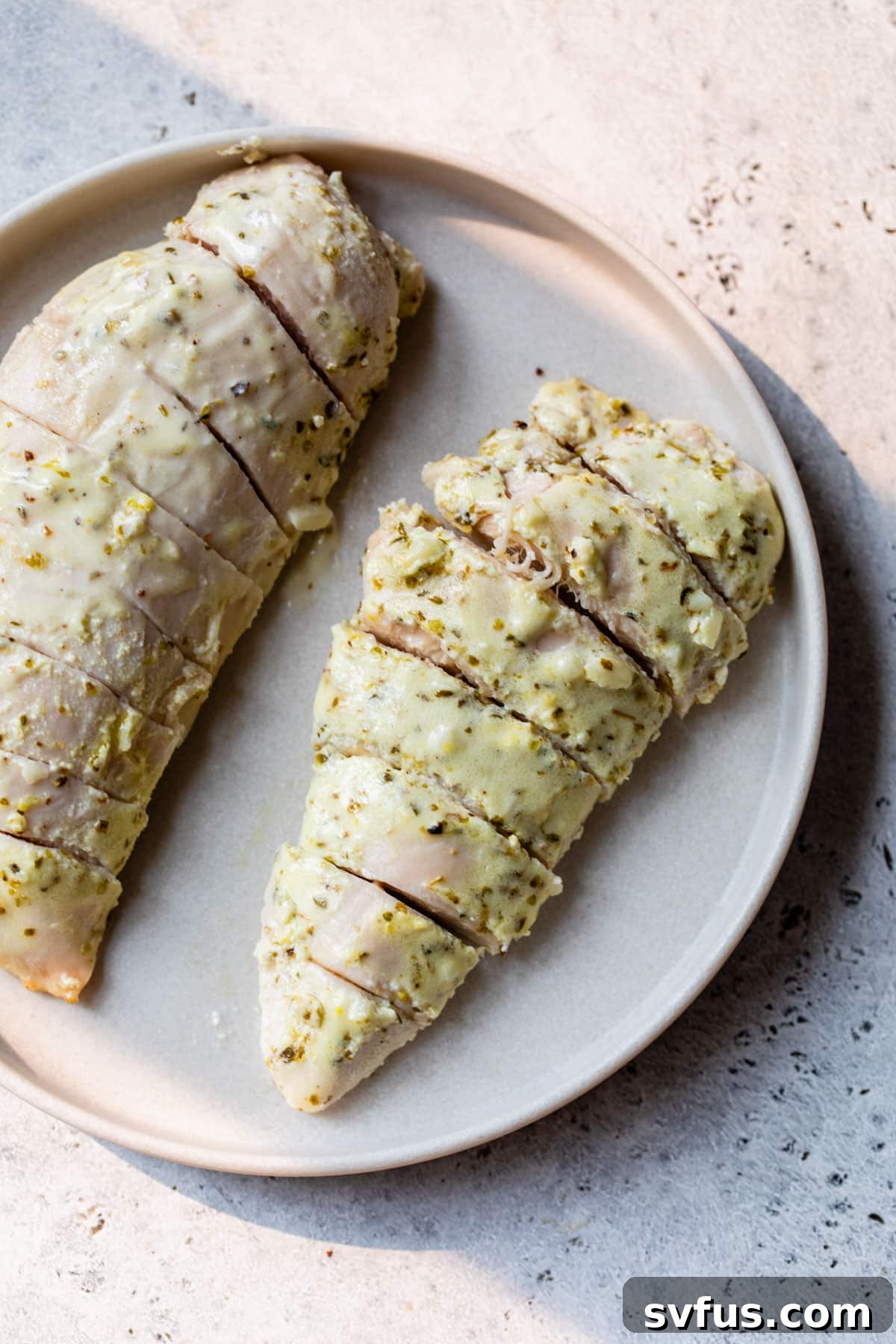 Two perfectly cooked and sliced Greek chicken breasts elegantly arranged on a serving plate, highlighting their tender texture and flavorful seasoning.
