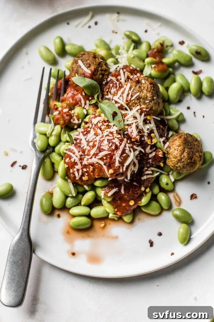 Overhead view of a vibrant plate of 10-minute meatless meatballs, edamame, and marinara sauce, garnished with fresh basil and chili flakes.