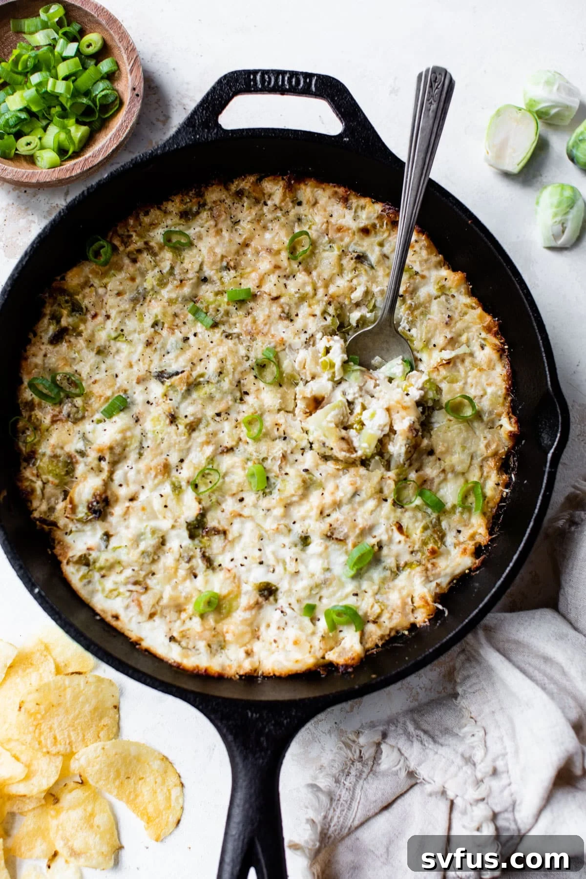 Hot Brussels Sprouts Dip baked in a cast iron skillet, served with a spoon ready for dipping