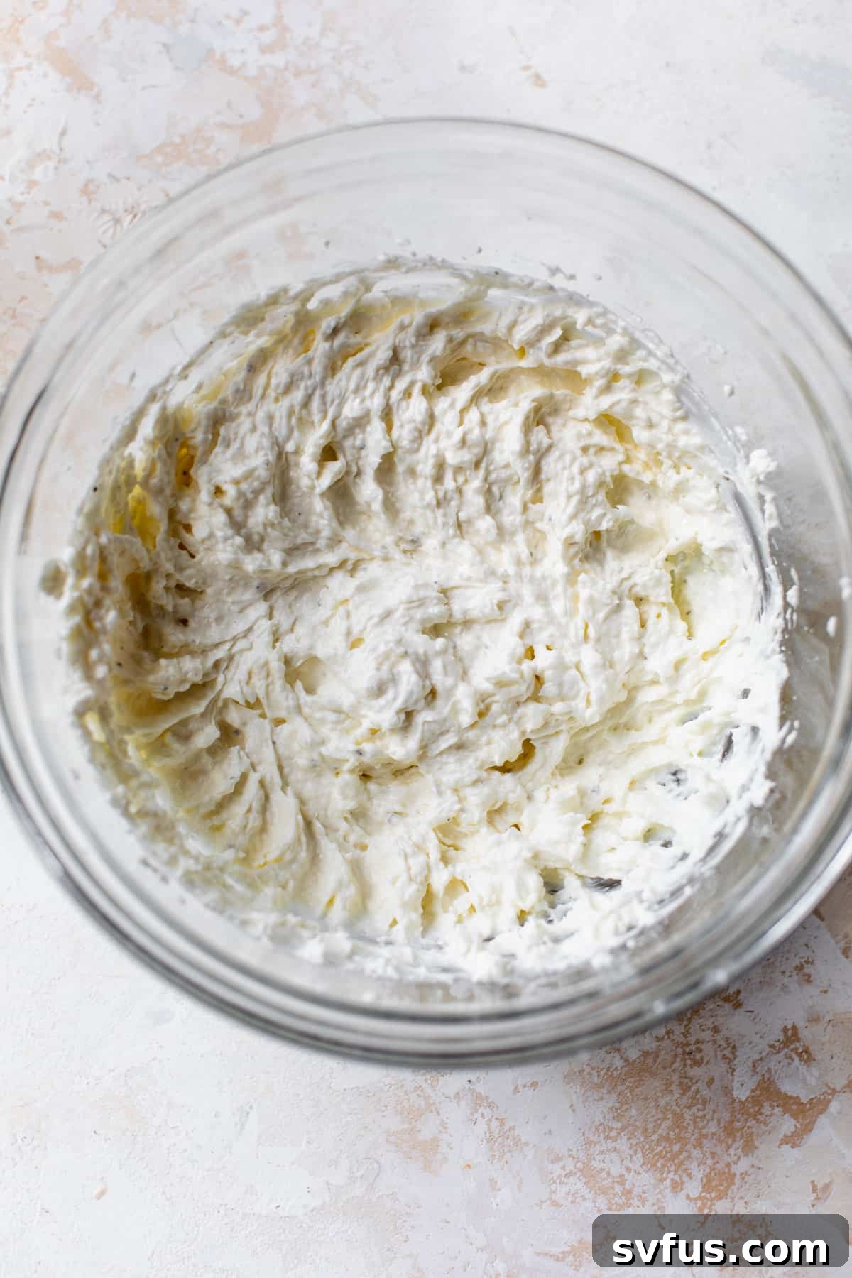 Cream cheese, yogurt, and shredded cheese mixed together in a glass bowl, ready for the sautéed vegetables