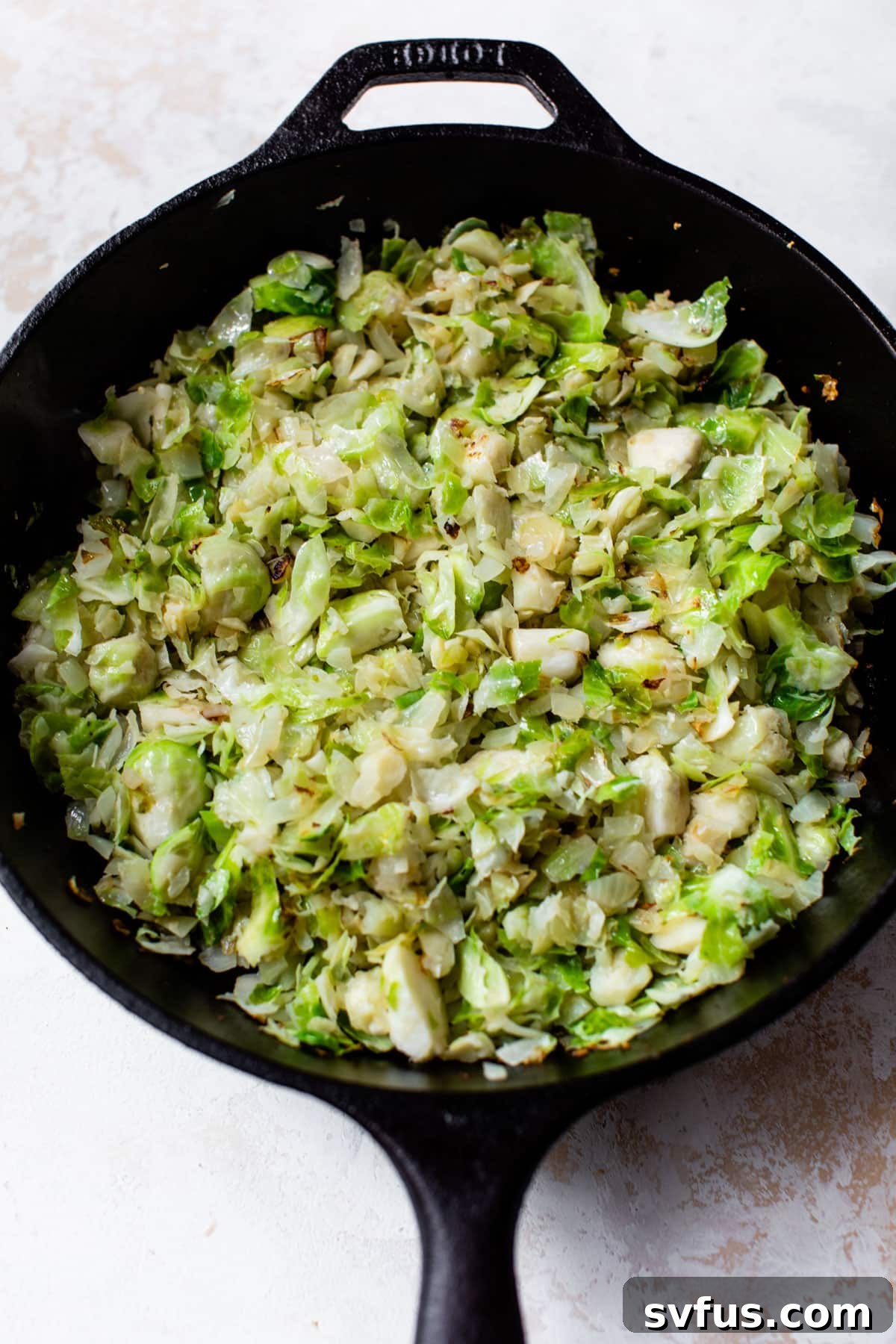 Chopped Brussels sprouts, garlic, and onion cooking in a cast iron skillet until tender