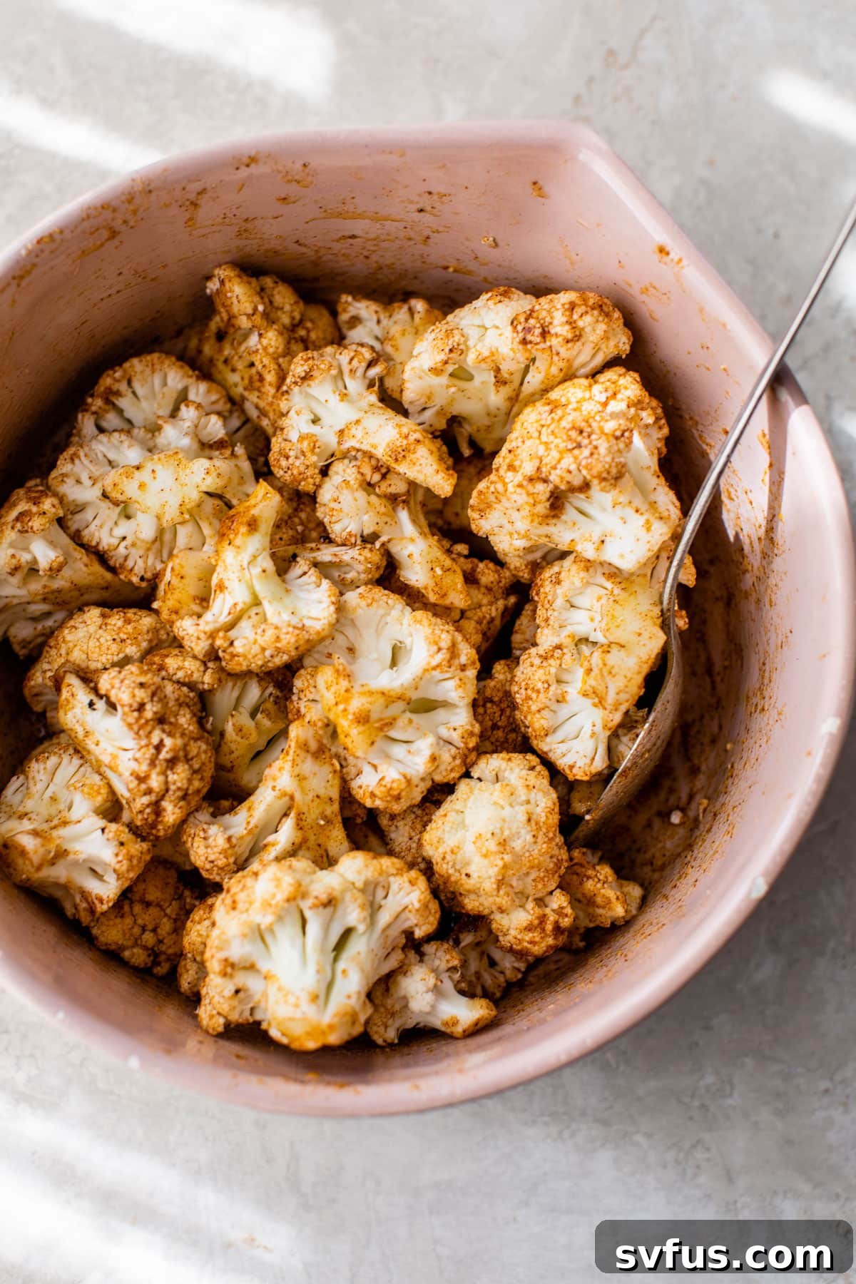 Cauliflower florets tossed with olive oil and a spicy seasoning blend in a bowl