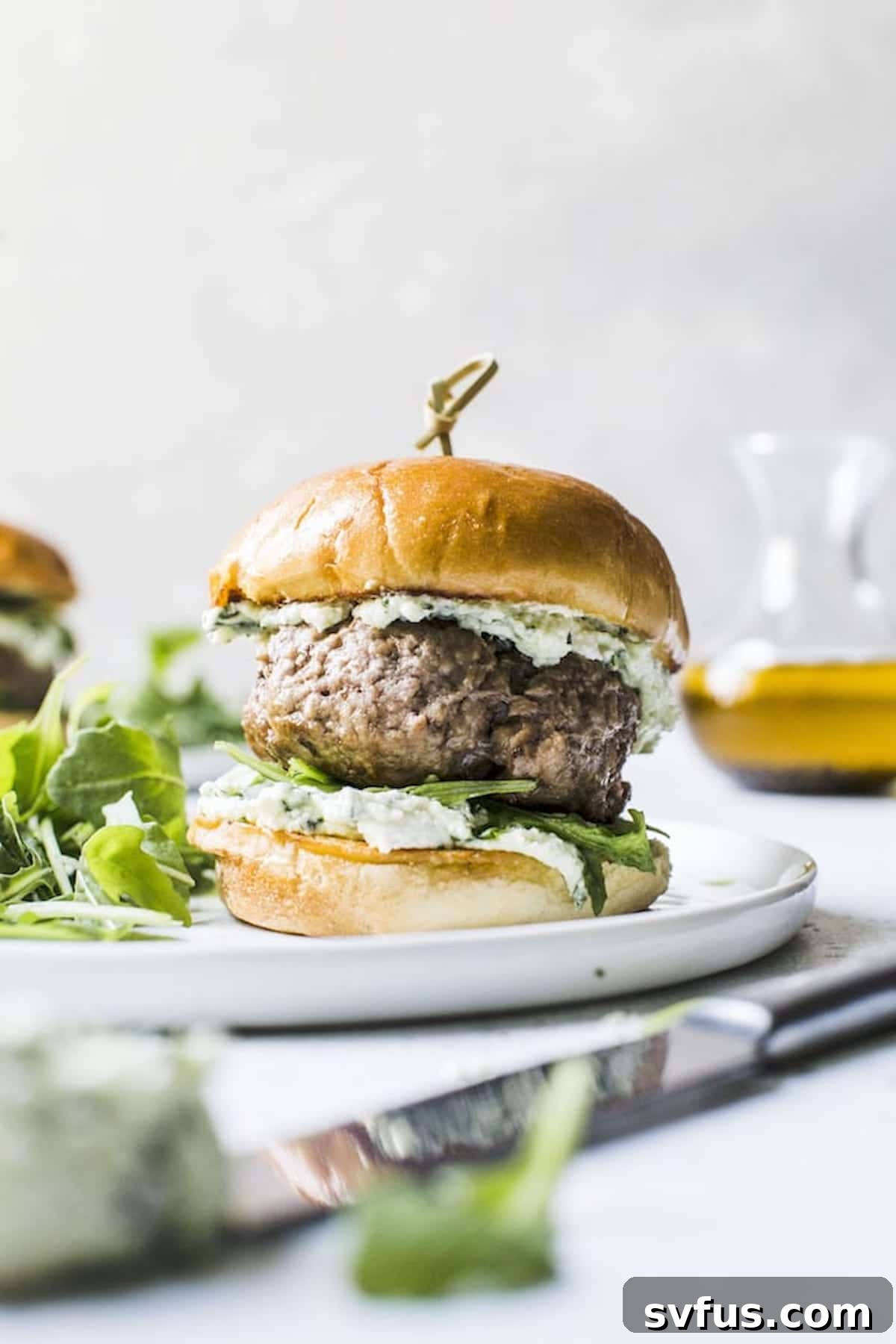 Grilled lamb burger on a plate with pesto whipped feta and fresh herbs