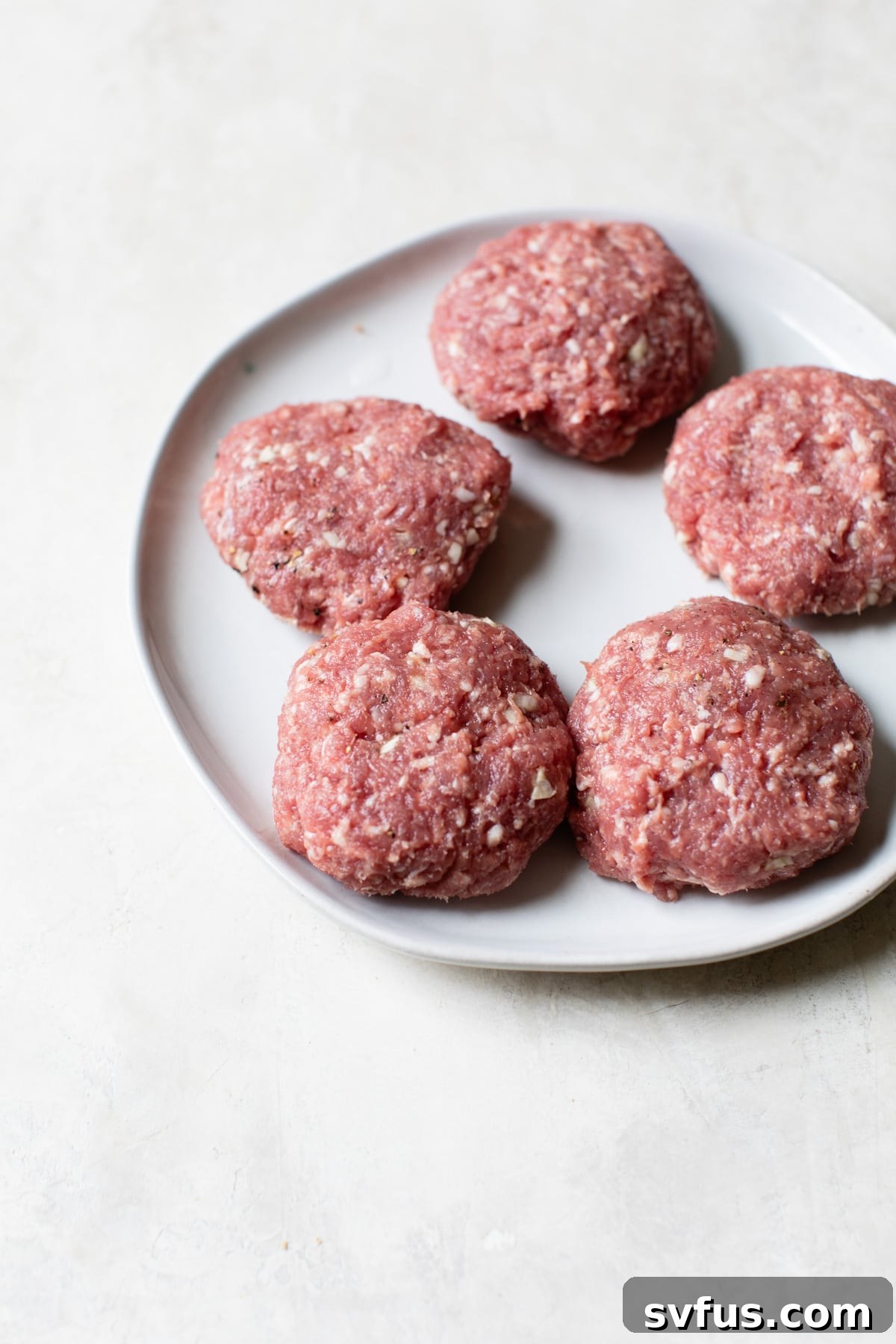 Uncooked lamb burger patties on a plate, ready for cooking