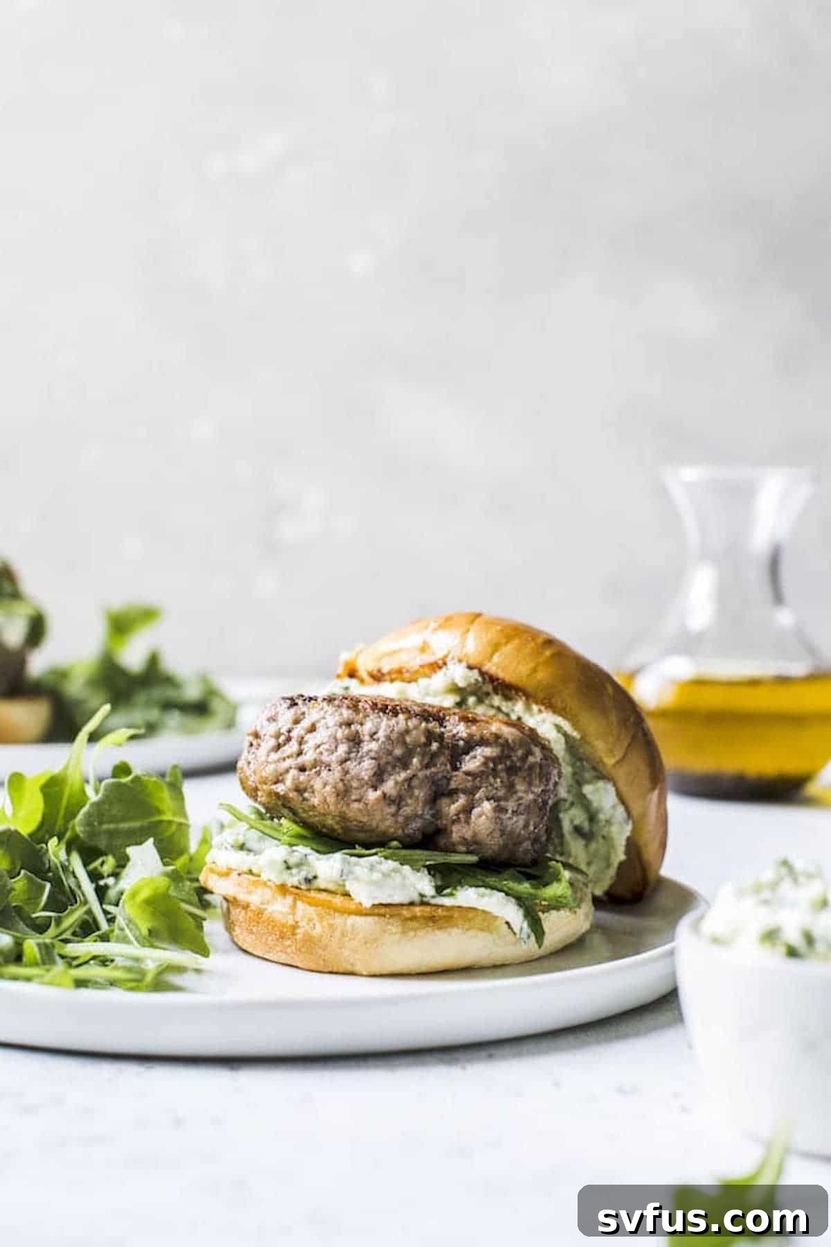 Close-up of a lamb burger with pesto whipped feta on a bun, served with various accompaniments