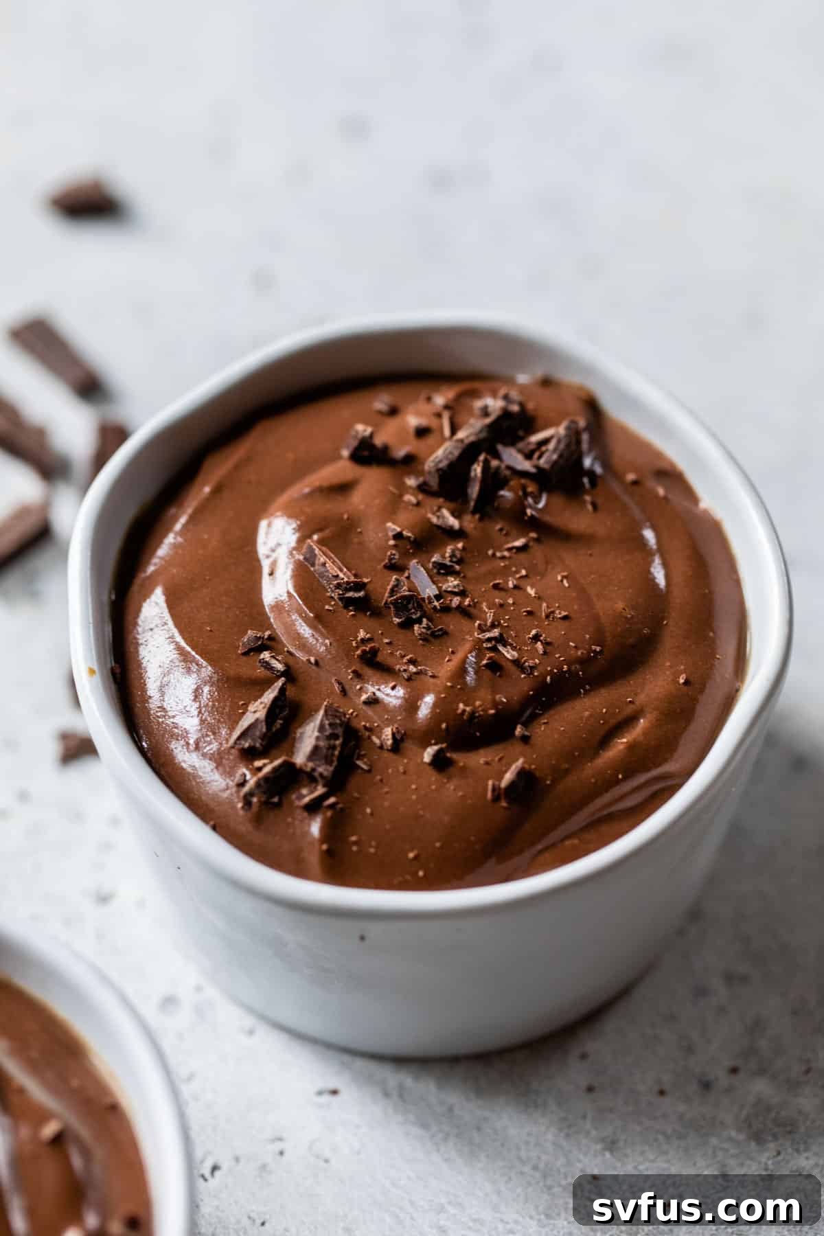 A delicate serving of vegan chocolate mousse, beautifully presented in a small white ramekin and garnished with elegant chocolate shavings on top.