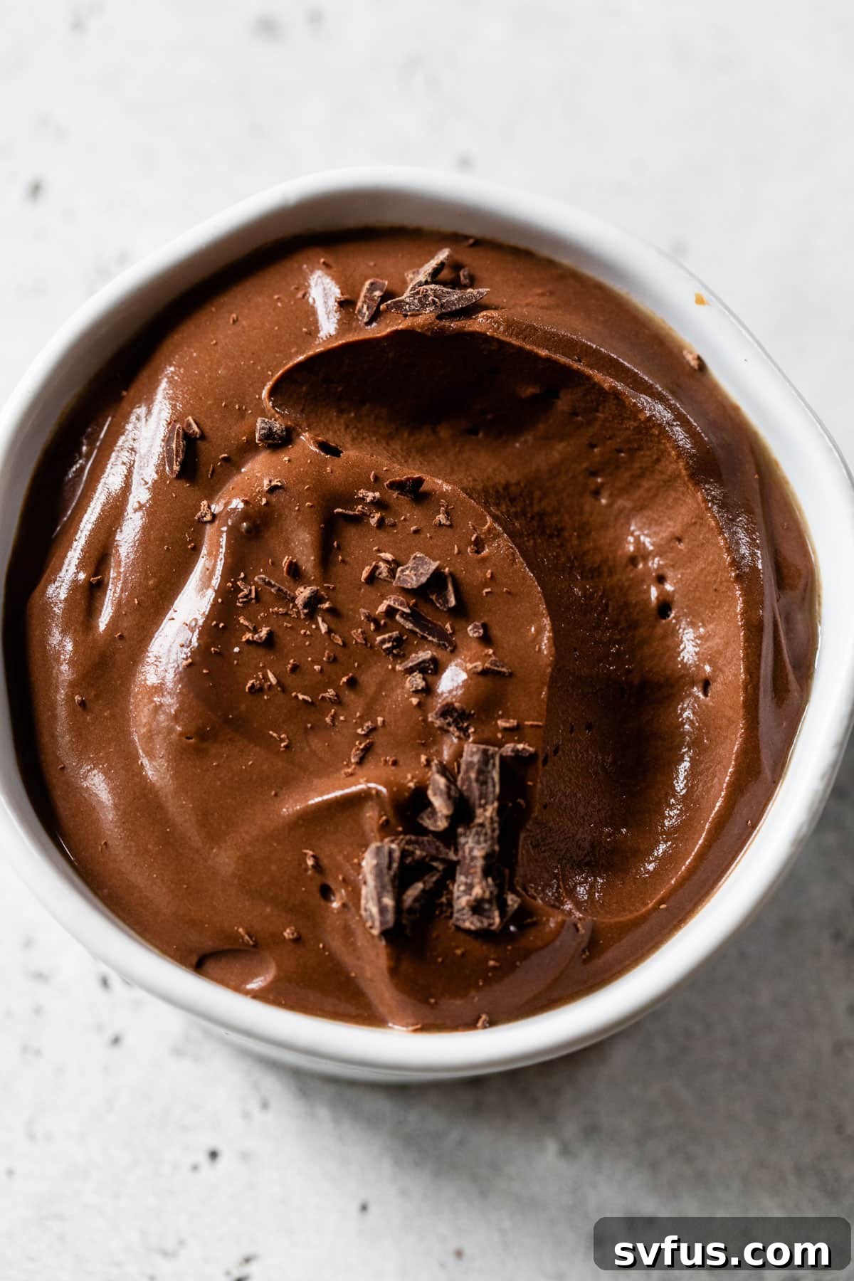 A close-up shot of a creamy vegan chocolate mousse served in a white bowl, with a small portion scooped out, showcasing its exquisite smooth and airy texture.