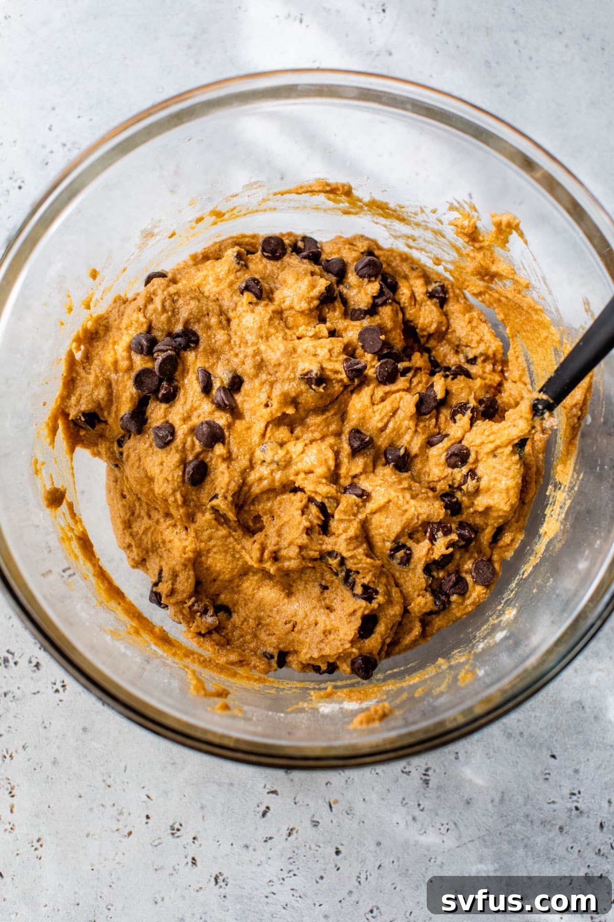A glass bowl of pumpkin chocolate chip muffin batter, rich and ready for baking.