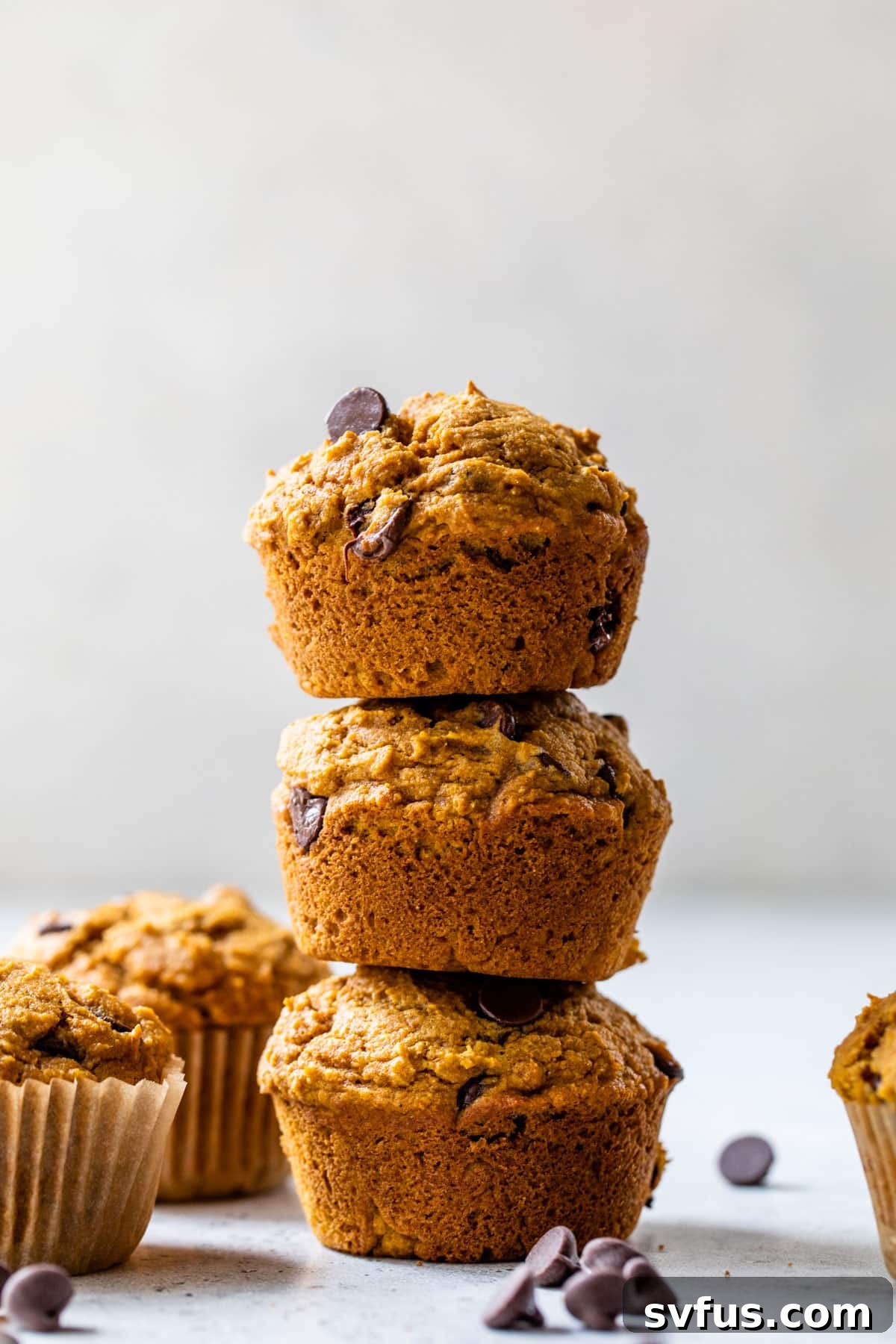 A side-view of three pumpkin chocolate chip muffins stacked on top of each other, showcasing their height and appealing texture.
