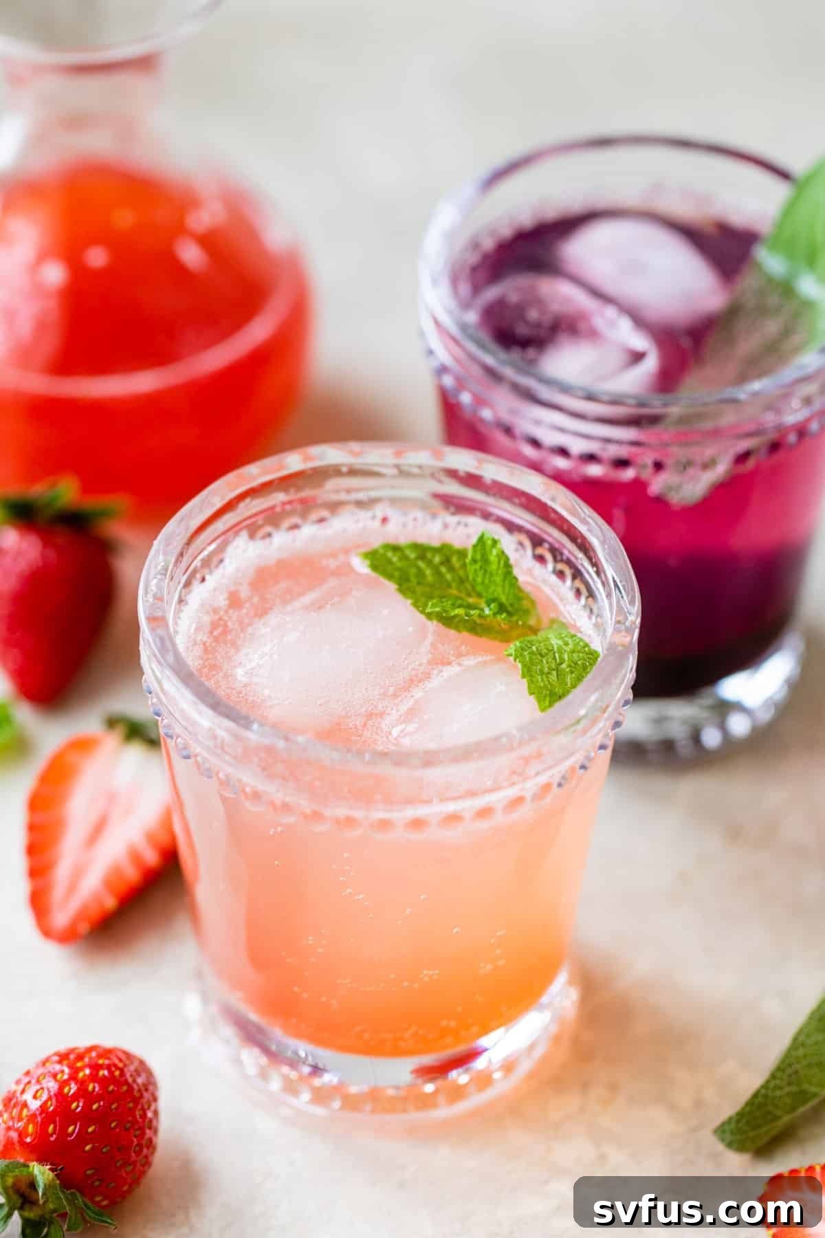 Two cocktail glasses filled with fruity drinks beside fresh strawberries and blackberries, showcasing a vibrant and refreshing beverage.