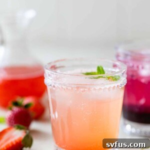two cocktail glasses with fruity drinks in them besides fresh strawberries and fresh blackberries