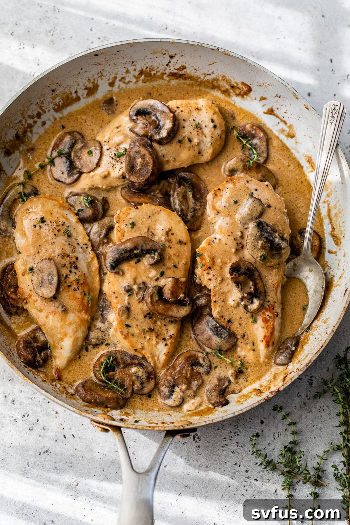 four chicken breasts in a skillet with a creamy mushroom sauce and fresh thyme