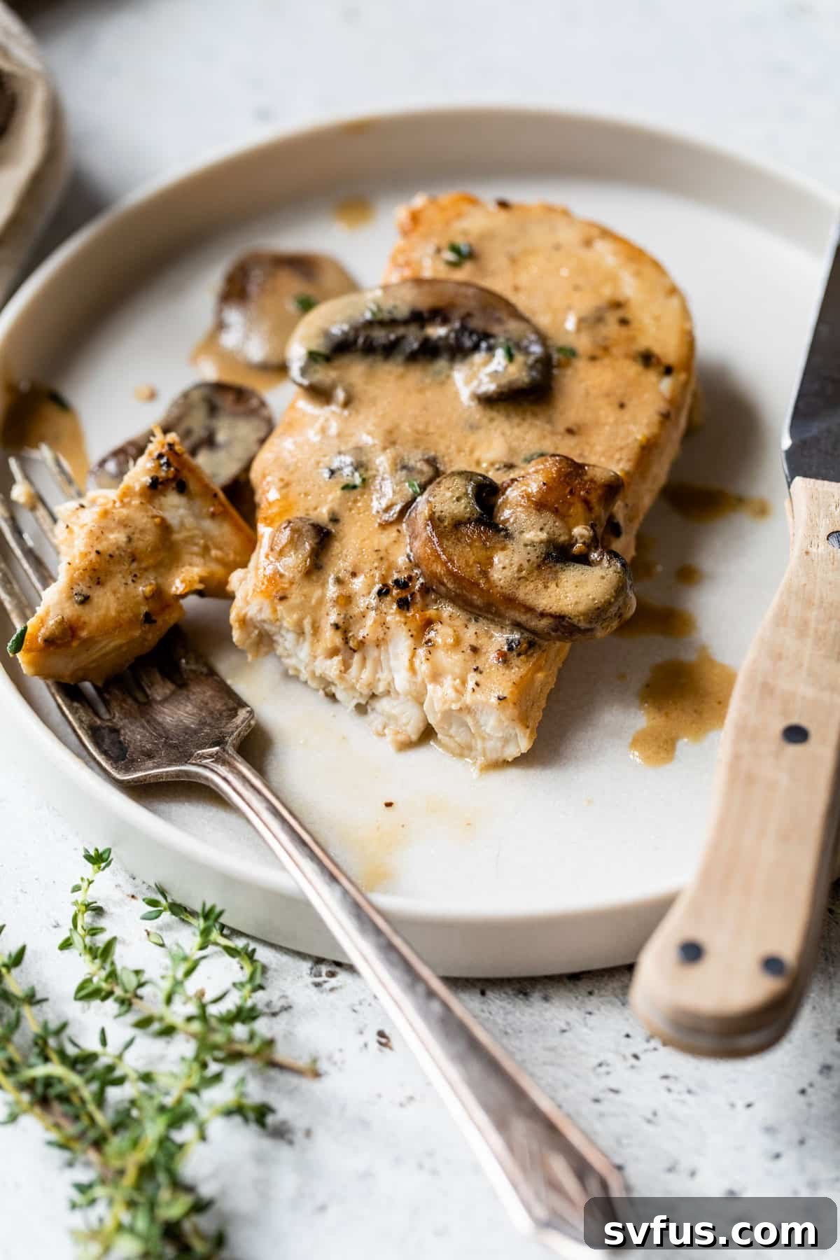 cooked chicken breast on a plate with mushroom sauce being cut with a fork and knife