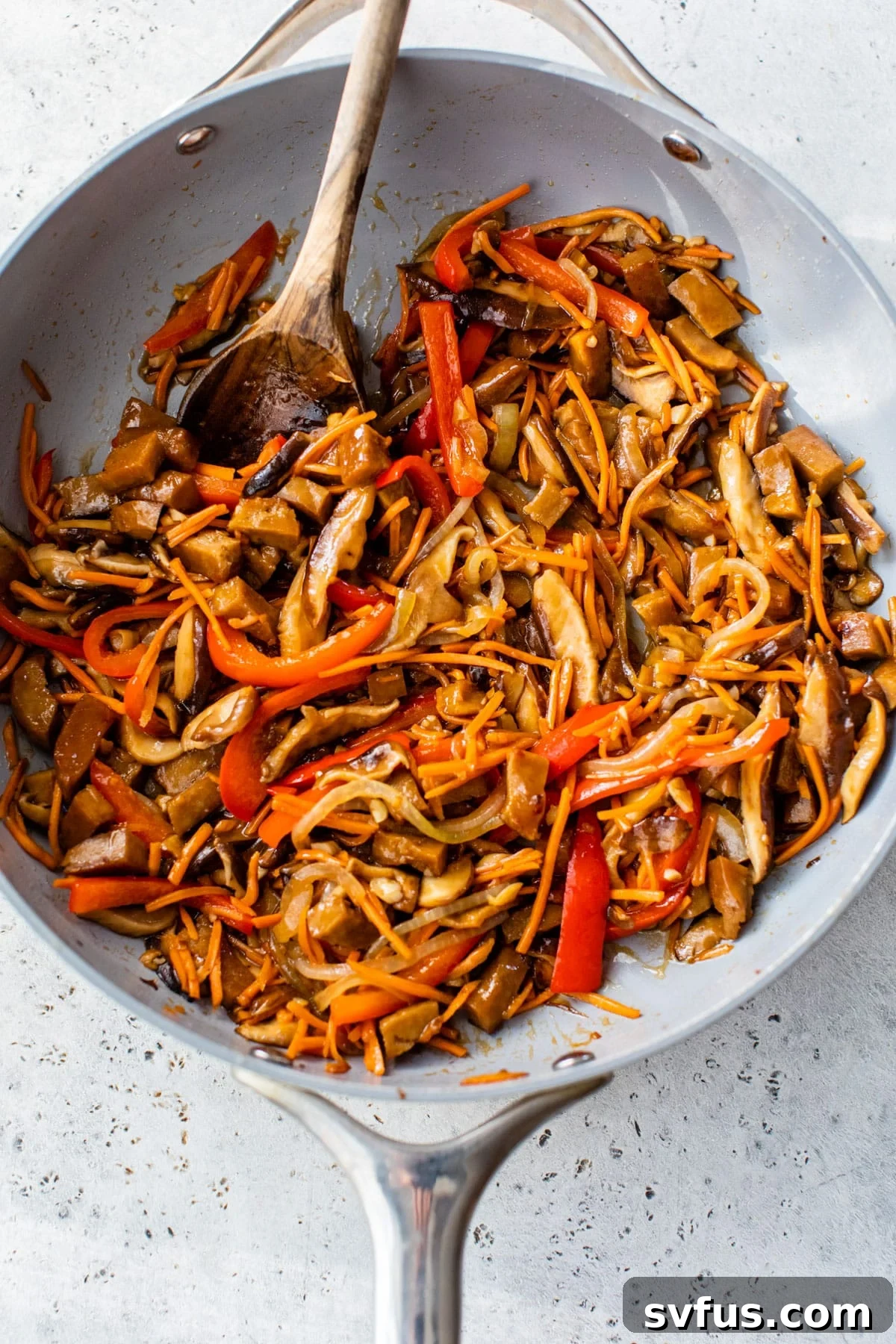 carrots, onion, peppers, and mushrooms cooking in a large skillet with a wooden spoon
