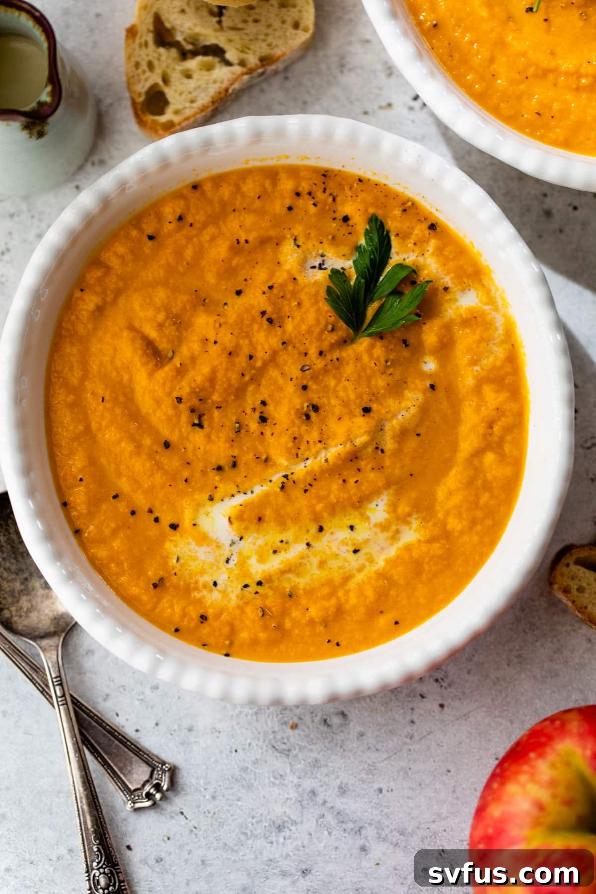 A beautifully presented bowl of creamy orange carrot apple ginger soup, garnished with fresh parsley and a delicate swirl of cream, inviting a sense of warmth and comfort.