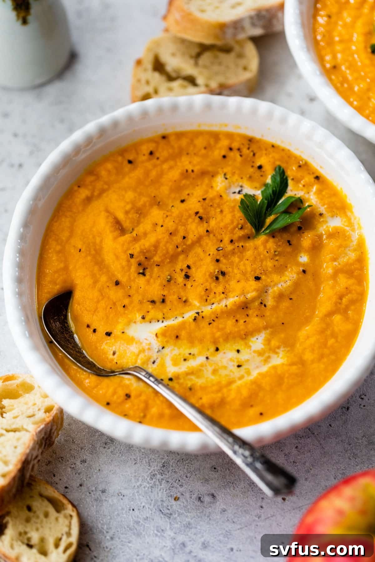 A vibrant bowl of pureed orange soup, featuring a spoon resting in it and topped with a sprinkle of fresh green parsley, ready to be enjoyed.
