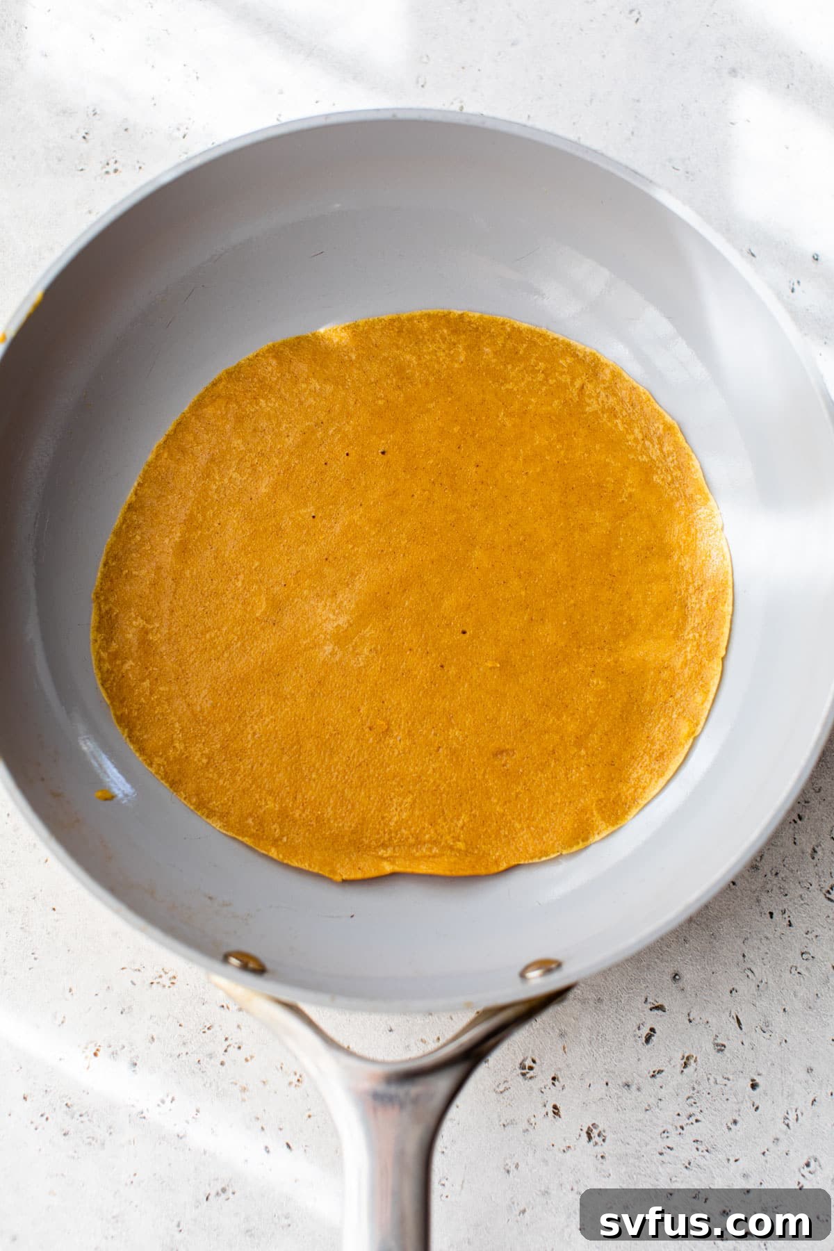 A thin, delicate pumpkin crepe cooking in a hot skillet, edges just beginning to crisp.