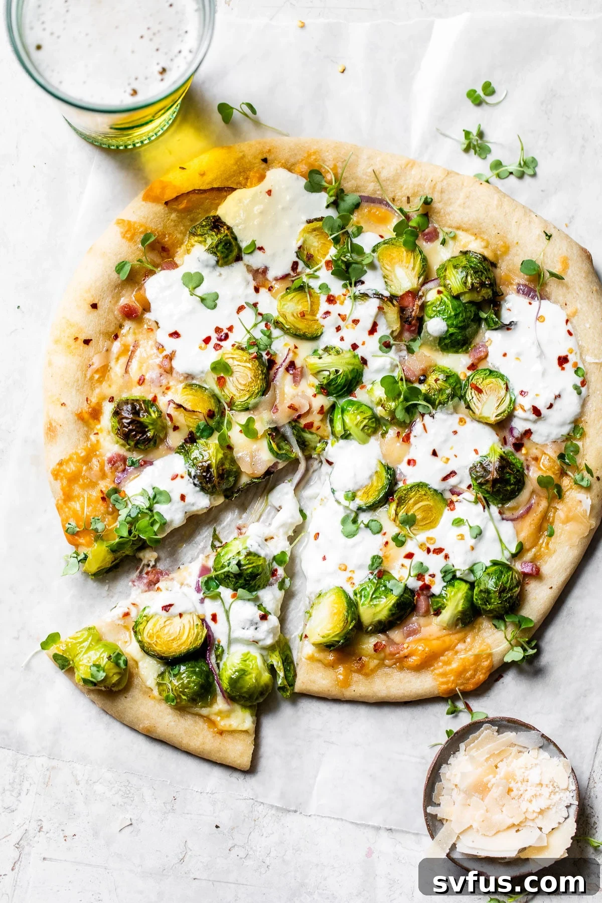 Delicious Brussels Sprouts Pizza with burrata and pancetta on parchment paper, served alongside a refreshing glass of beer.