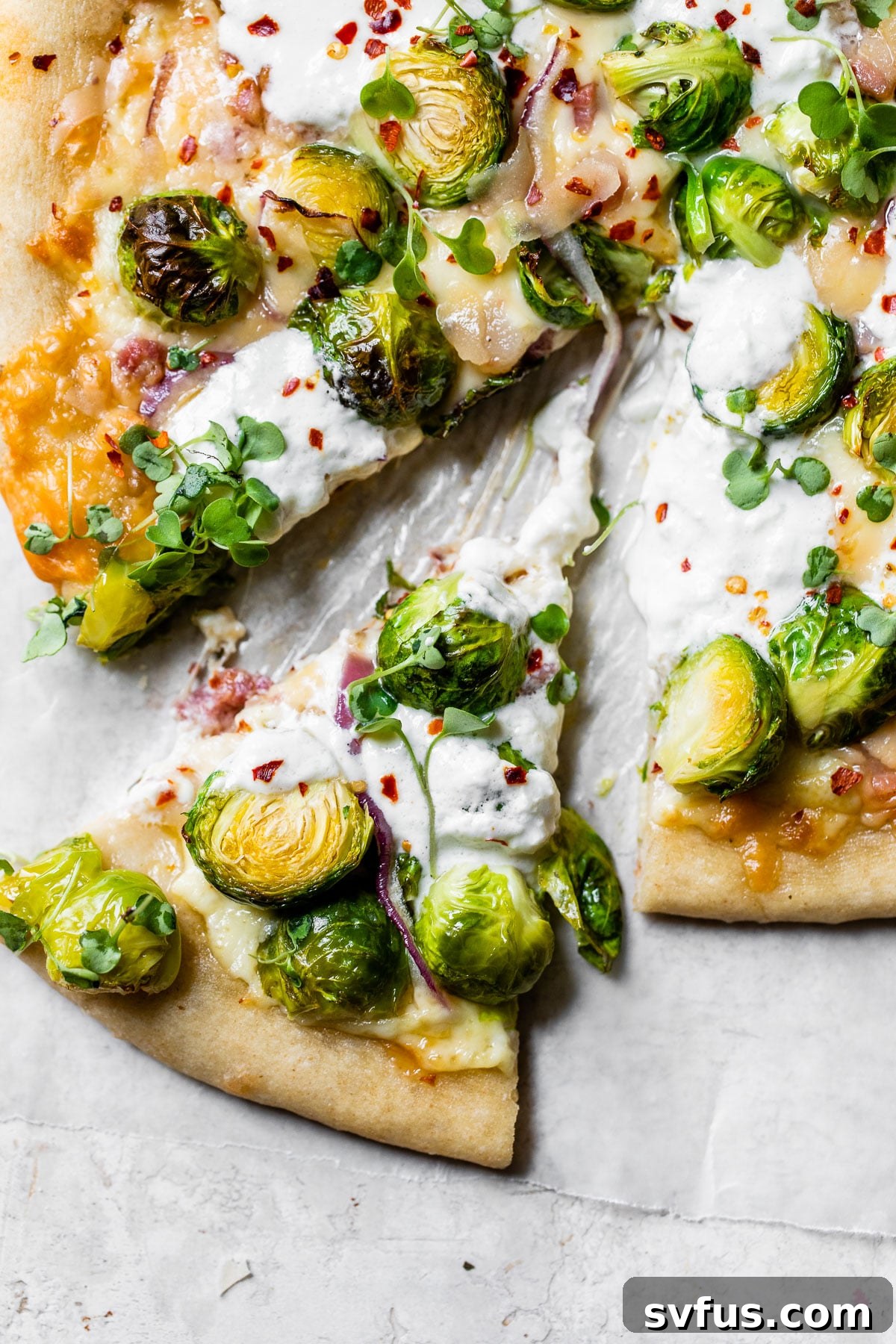 A perfectly baked slice of Brussels Sprouts Pizza, featuring caramelized brussels sprouts, melted burrata, and crispy pancetta, ready to be enjoyed.