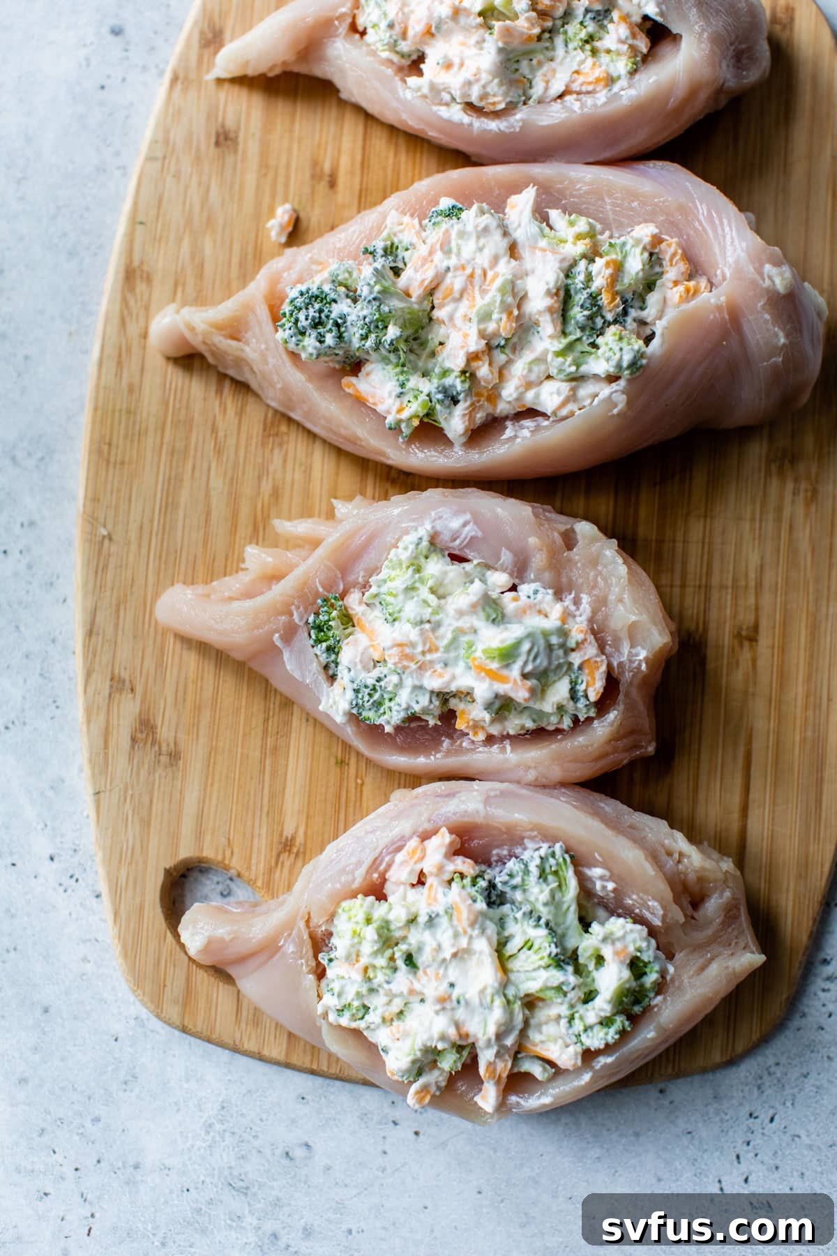 A raw chicken breast is shown on a cutting board, with the creamy broccoli cheddar filling inside, secured with toothpicks.