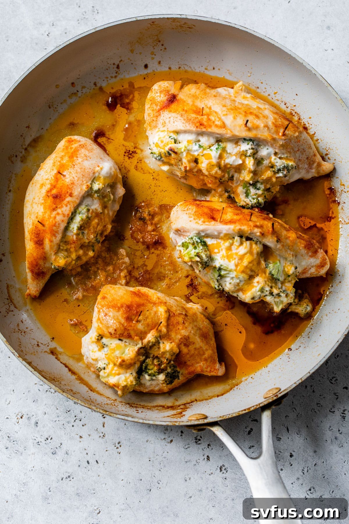 An overview of stuffed chicken breasts sizzling in a cast iron skillet on the stovetop.