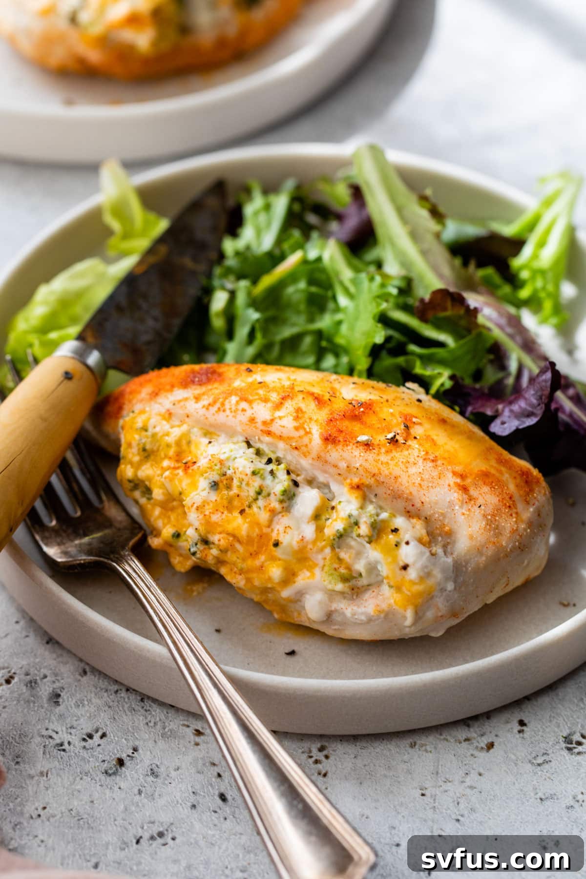 A close-up of a cooked and sliced stuffed chicken breast, showcasing the creamy filling, on a white plate with cutlery.