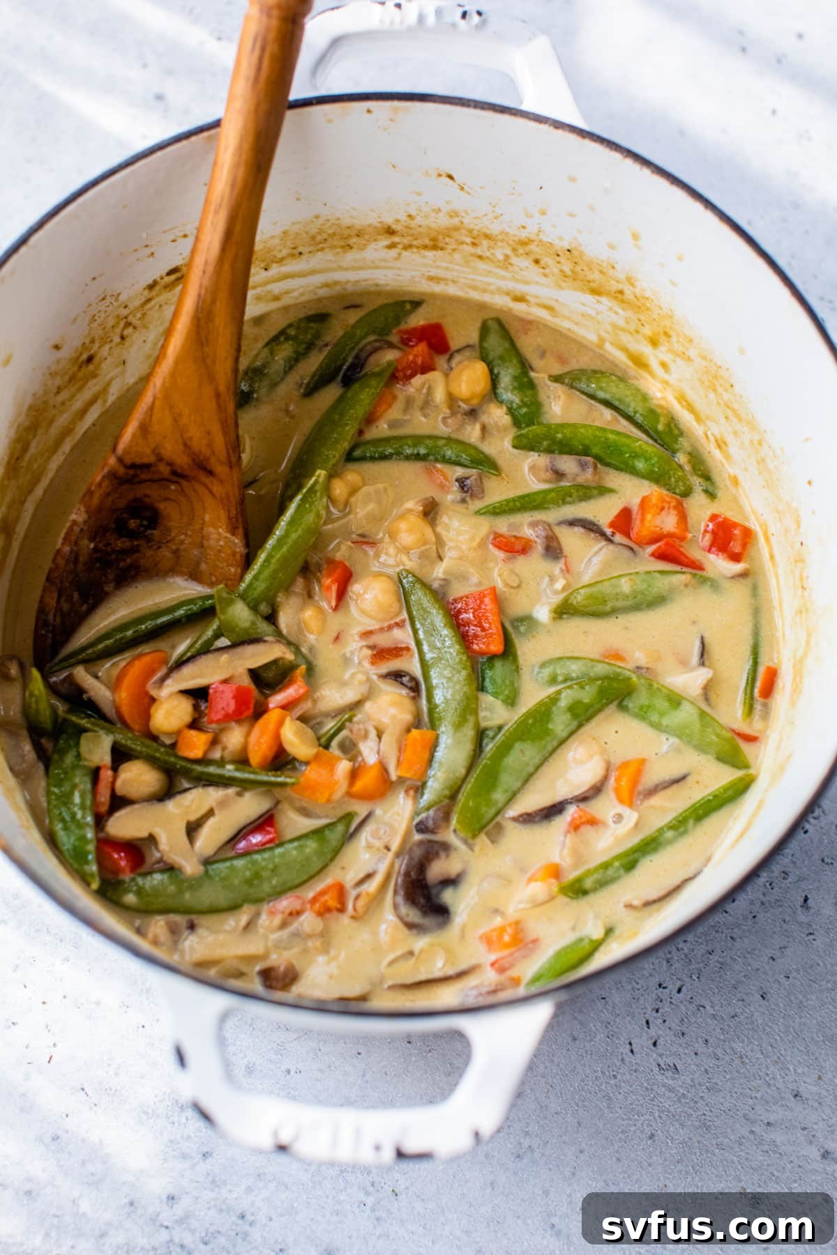 vegan green curry inside of a dutch oven with a wooden spoon