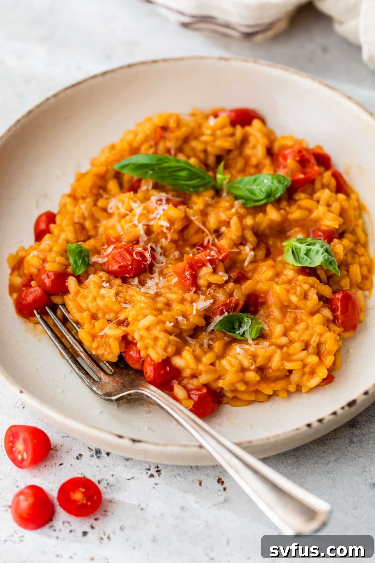 A close-up shot of a bowl of creamy tomato risotto with a fork, garnished with fresh tomatoes, basil leaves, and a sprinkle of grated Parmesan cheese.
