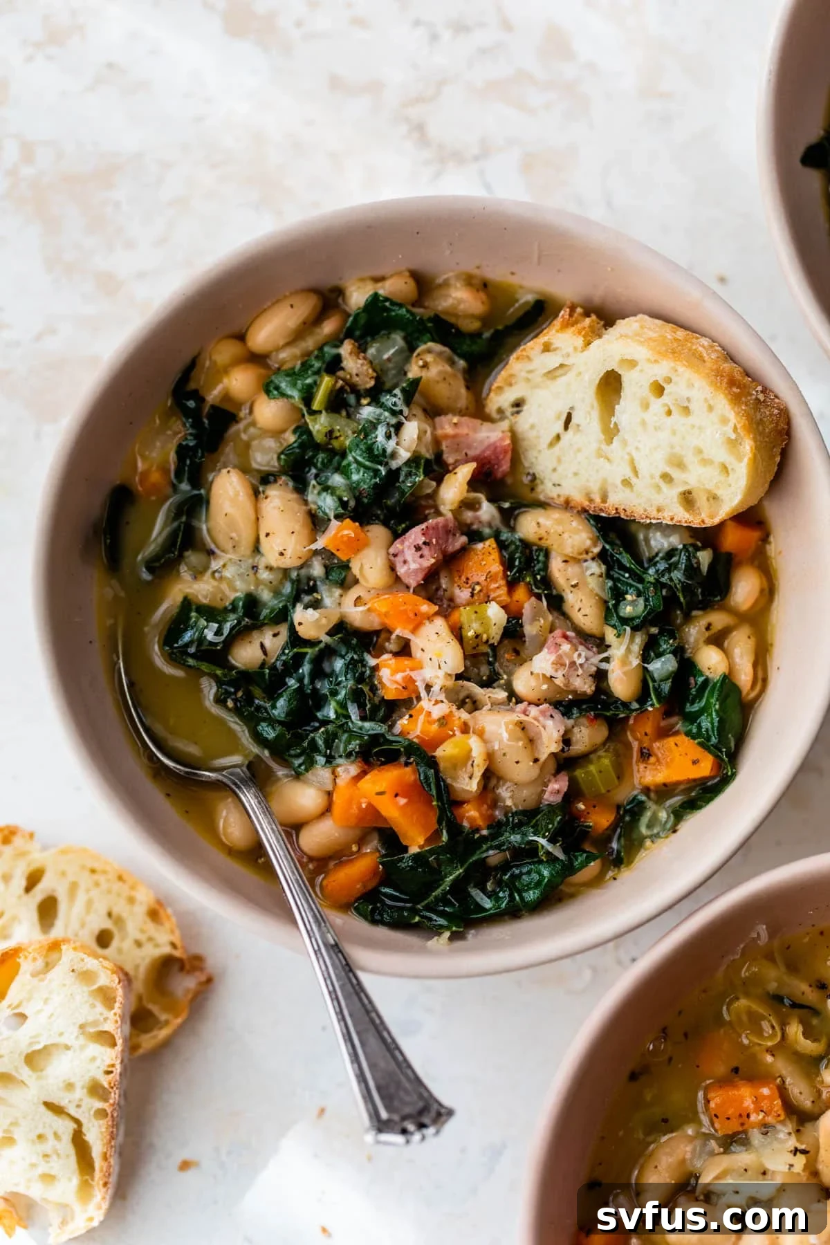 A steaming bowl of creamy white bean soup with a spoon and a slice of crusty bread, ready to be enjoyed.