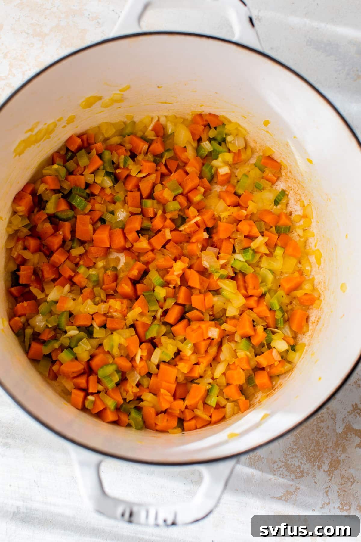 Diced celery, carrots, and onion sautéing in a Dutch oven, forming the aromatic base for the soup.