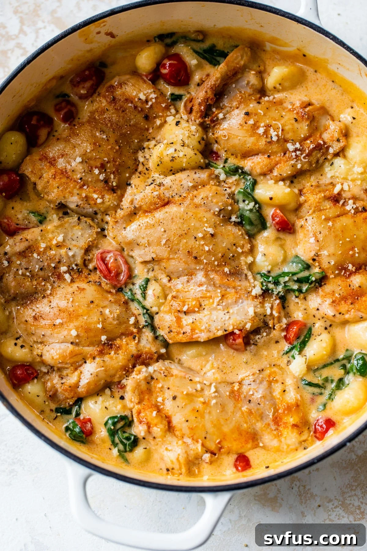 A large, deep skillet brimming with cooked chicken thighs, perfectly wilted spinach, vibrant halved grape tomatoes, and potato gnocchi, all swimming in a rich, creamy sauce.